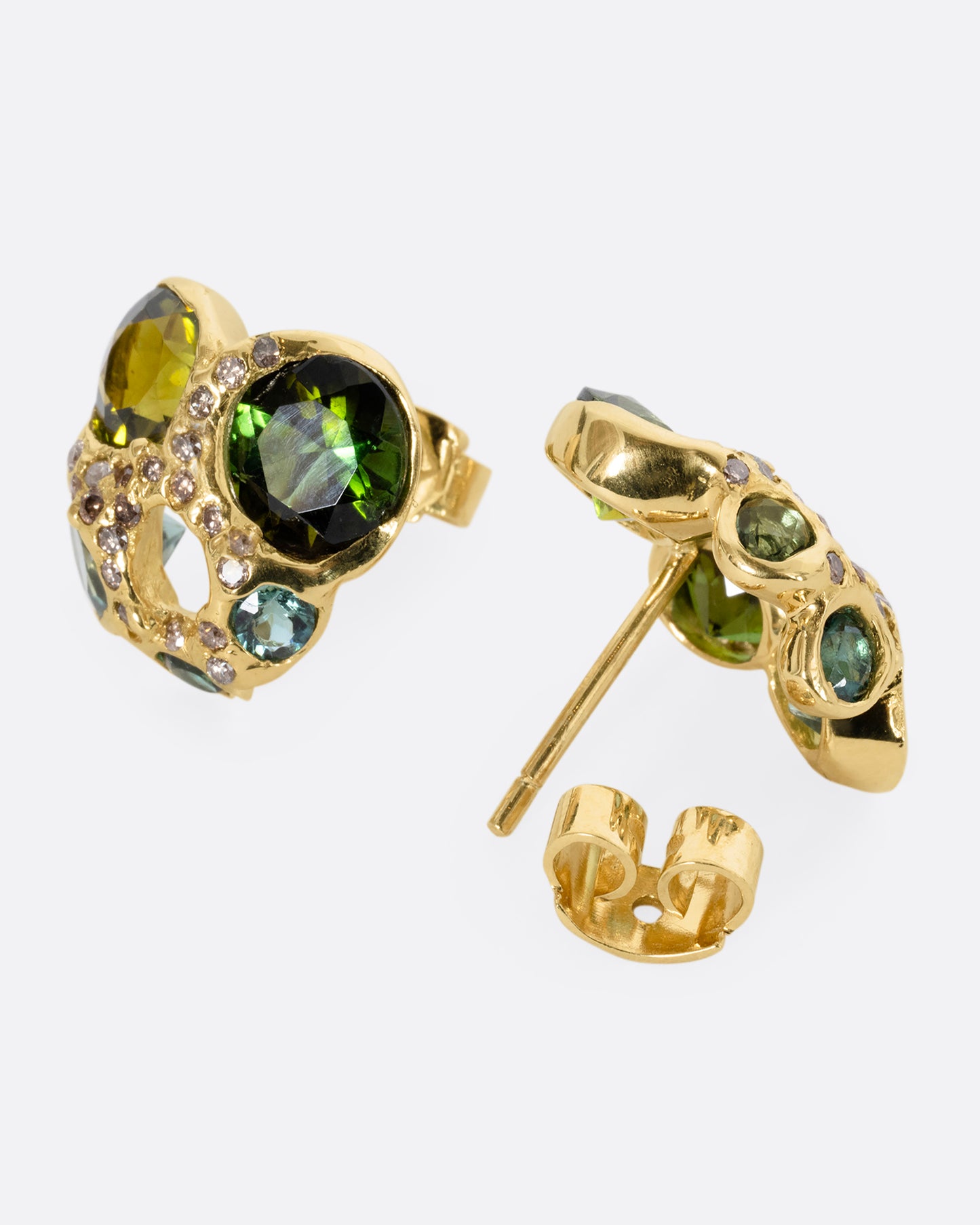 Yellow gold stud earrings with open centers and free- form tourmalines in varying shades of green. Tiny white diamonds are peppered throughout. One earring is shown on its side from the front. The other is shown open on its side from the back.