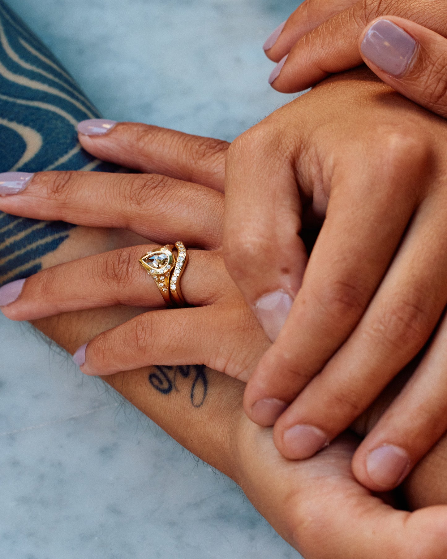 A close up of clasped hands, one with a thick curved band with nine flush-set diamonds. Shown from the front.