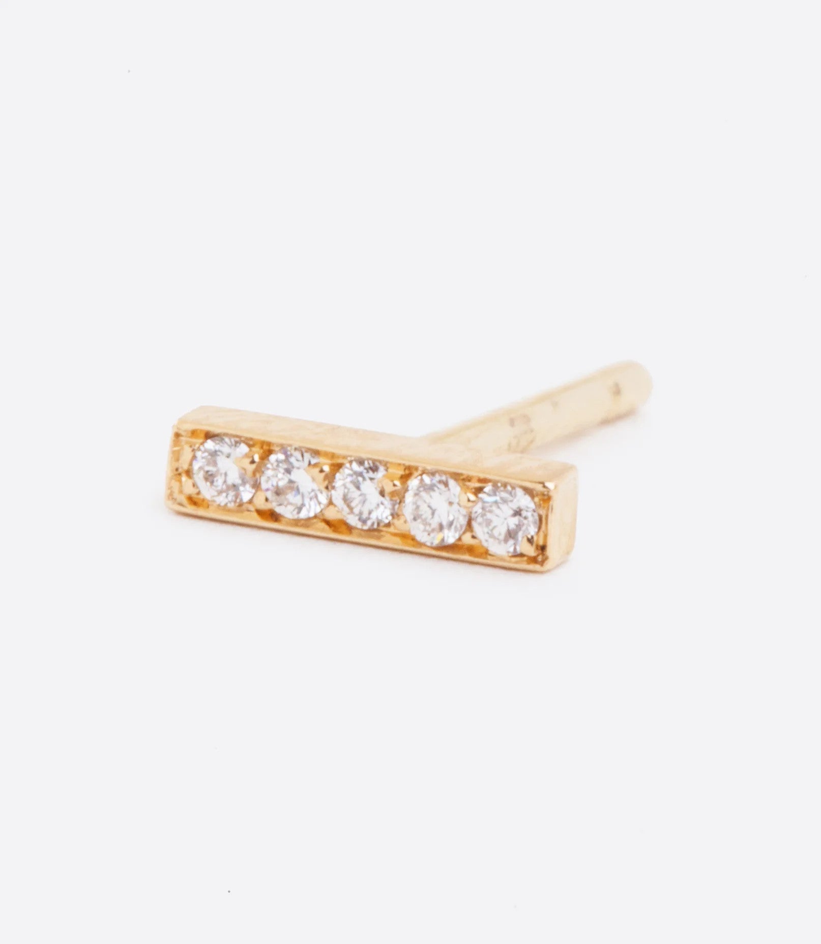 A yellow gold bar stud earring with five white diamonds. Shown lying on its side from the front.