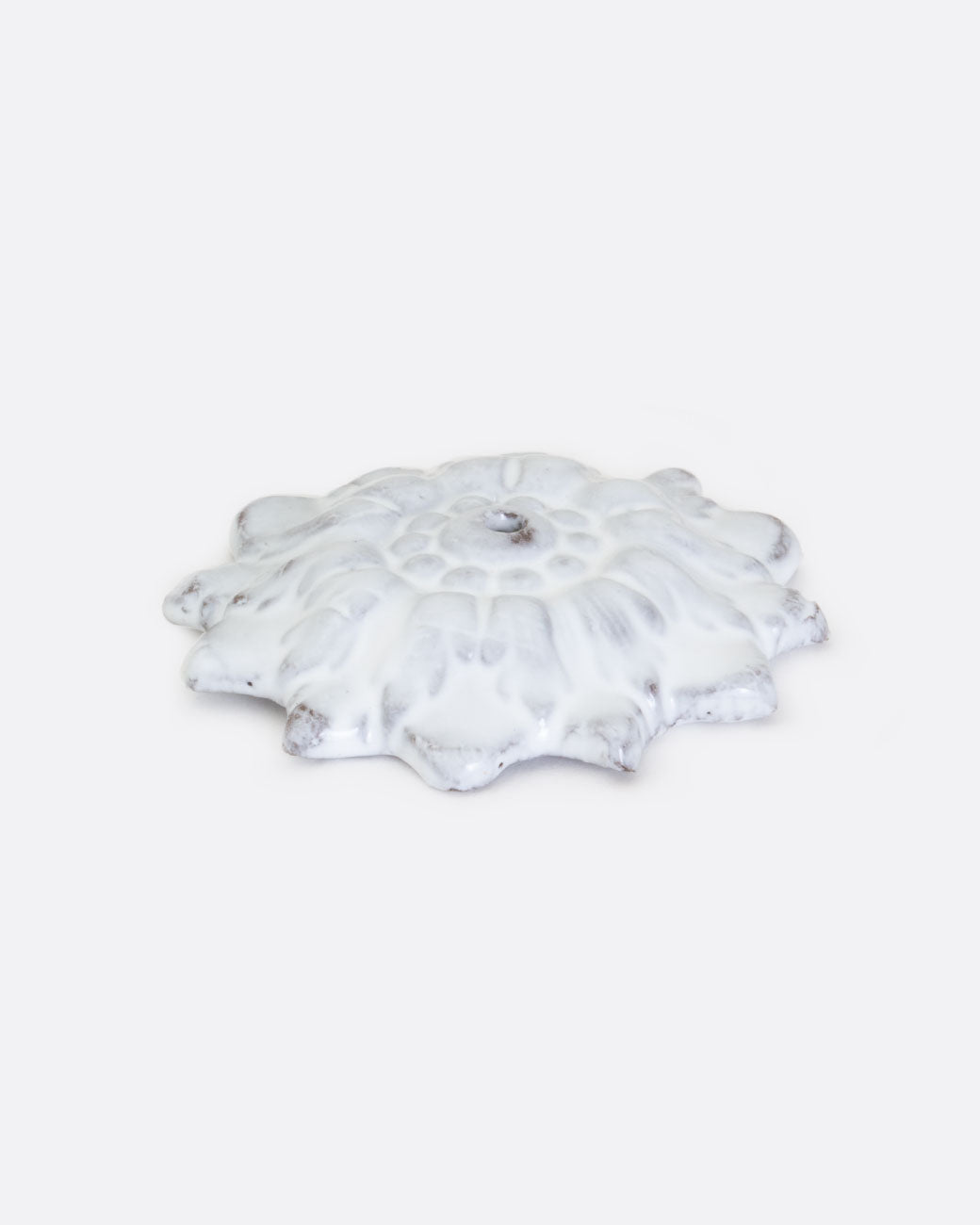 A white ceramic incense holder in the shape of a flower with a center hole. Shown lying flat from the front.