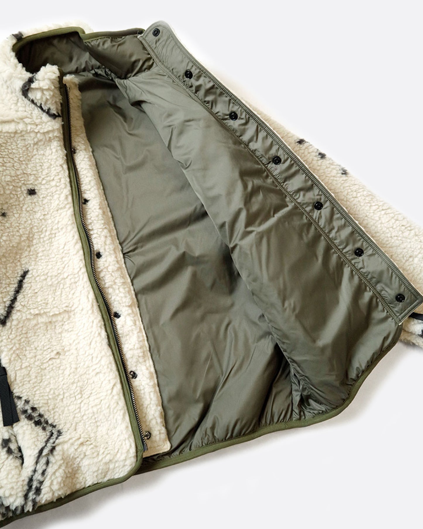 A reversible jacket with white Beni Ourain patterned fleece on one side and a green nylon shell on the other, shown lying flat unzipped so you can see the interior.