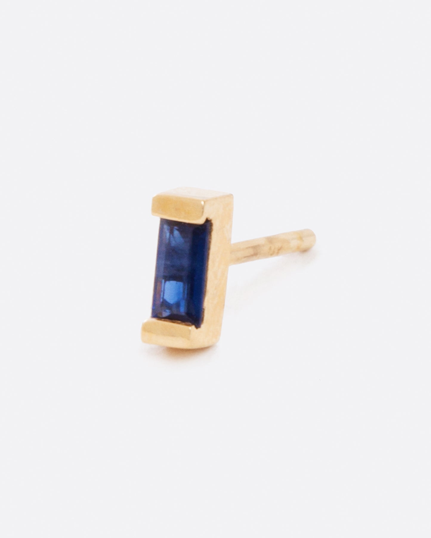 A single earring with a small blue sapphire baguette set in yellow gold. Shown diagonally shown from the side.