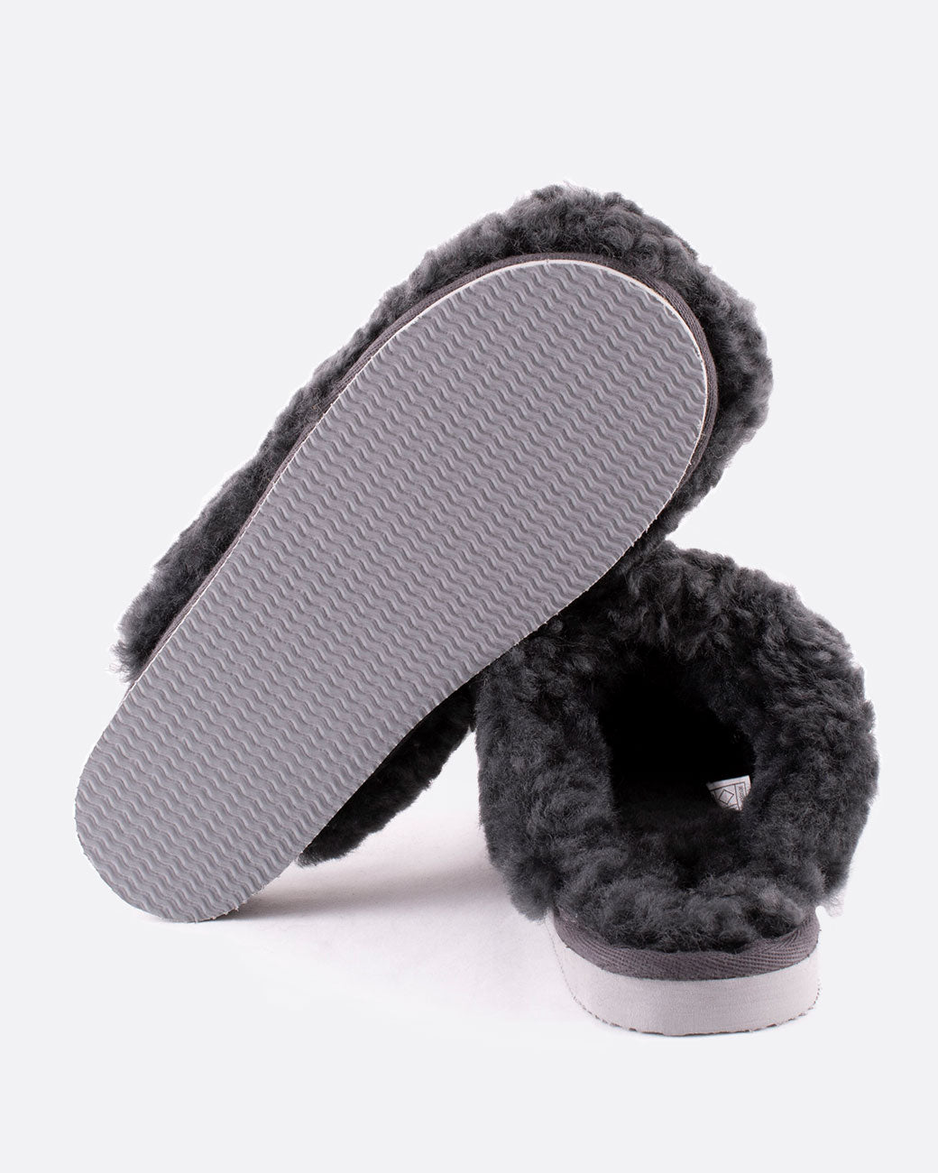 A pair of Jenny sheepskin slippers in charcoal gray. One slipper is shown from the bottom, the other is shown from the back.