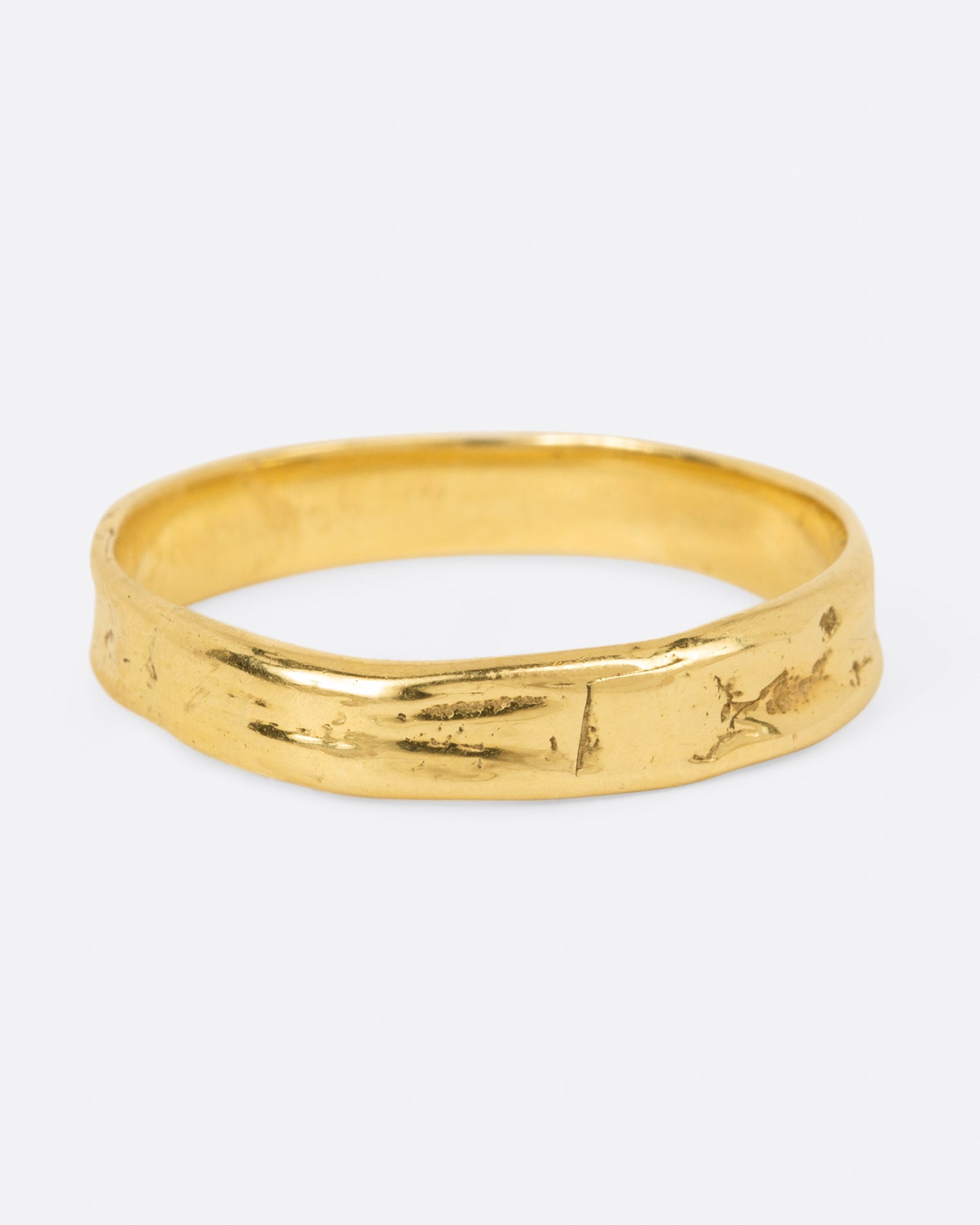 A textured yellow gold band that is meant to look worn in, shown from the side.