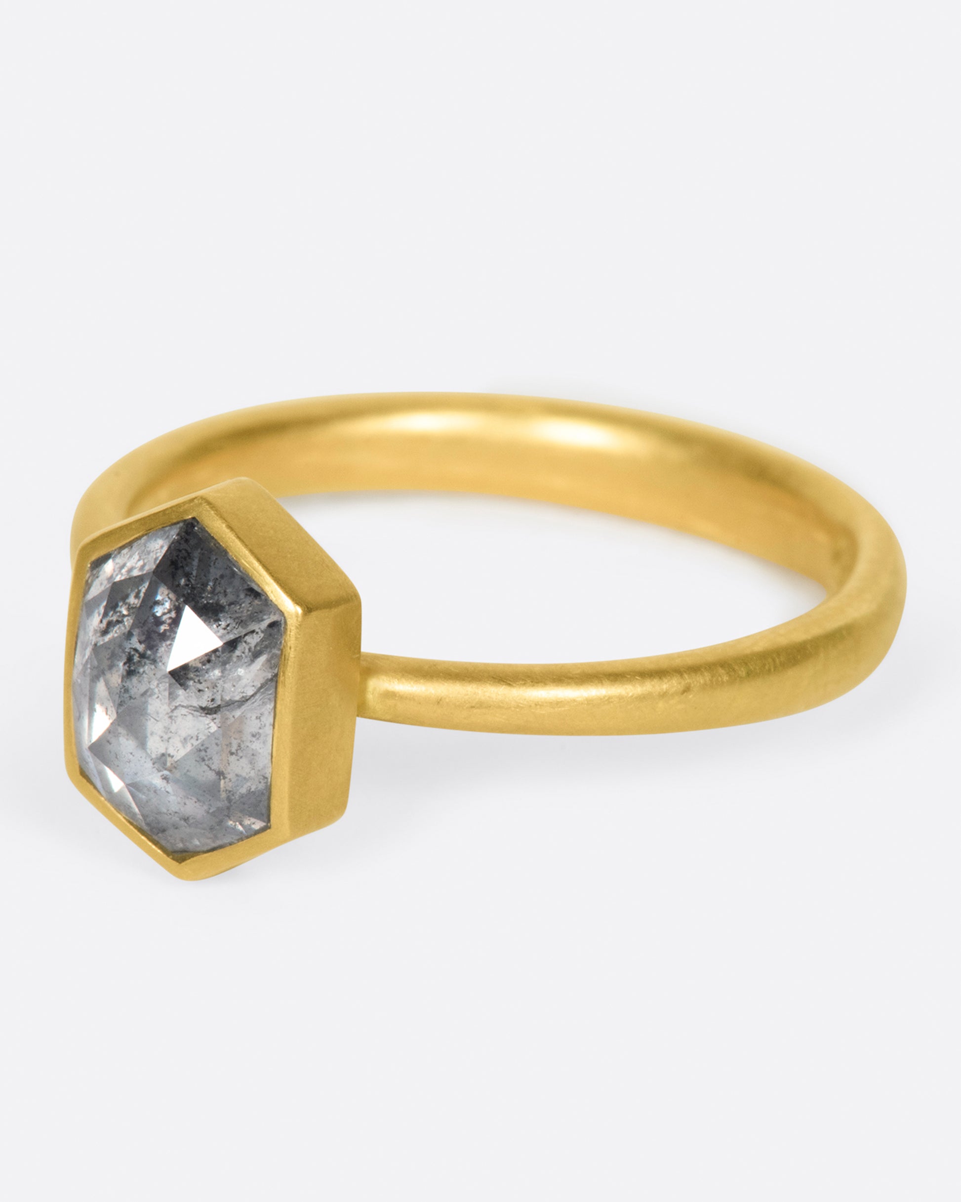 A yellow gold ring with a salt and pepper hexagonal diamond. Shown from the side.