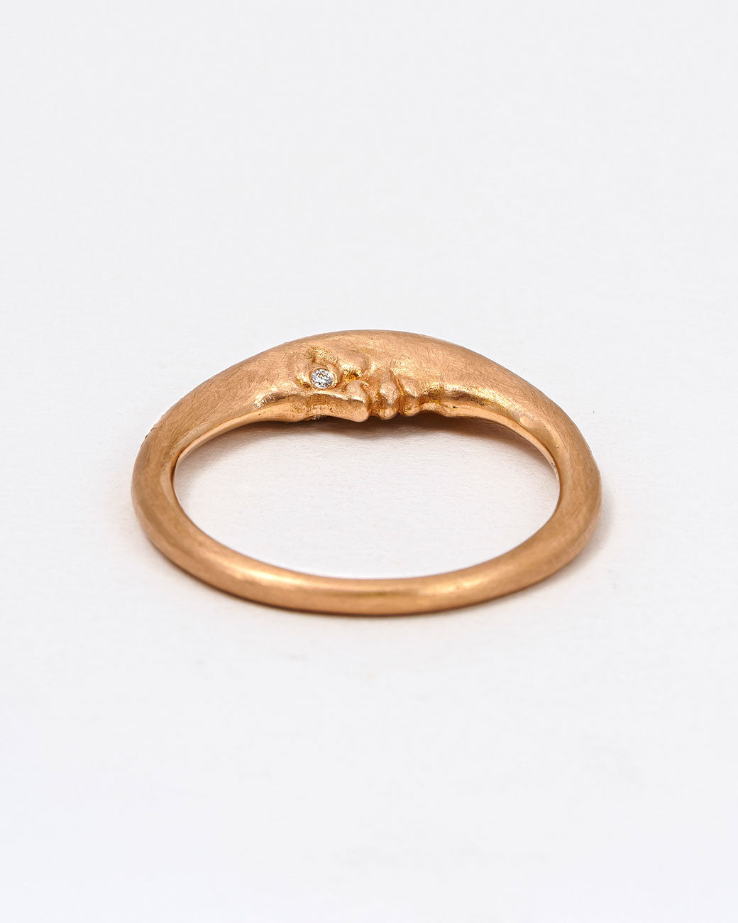 A rose gold crescent moon ring with a diamond eyed face and graduated white diamonds around the top edge. Shown lying flat from the side.