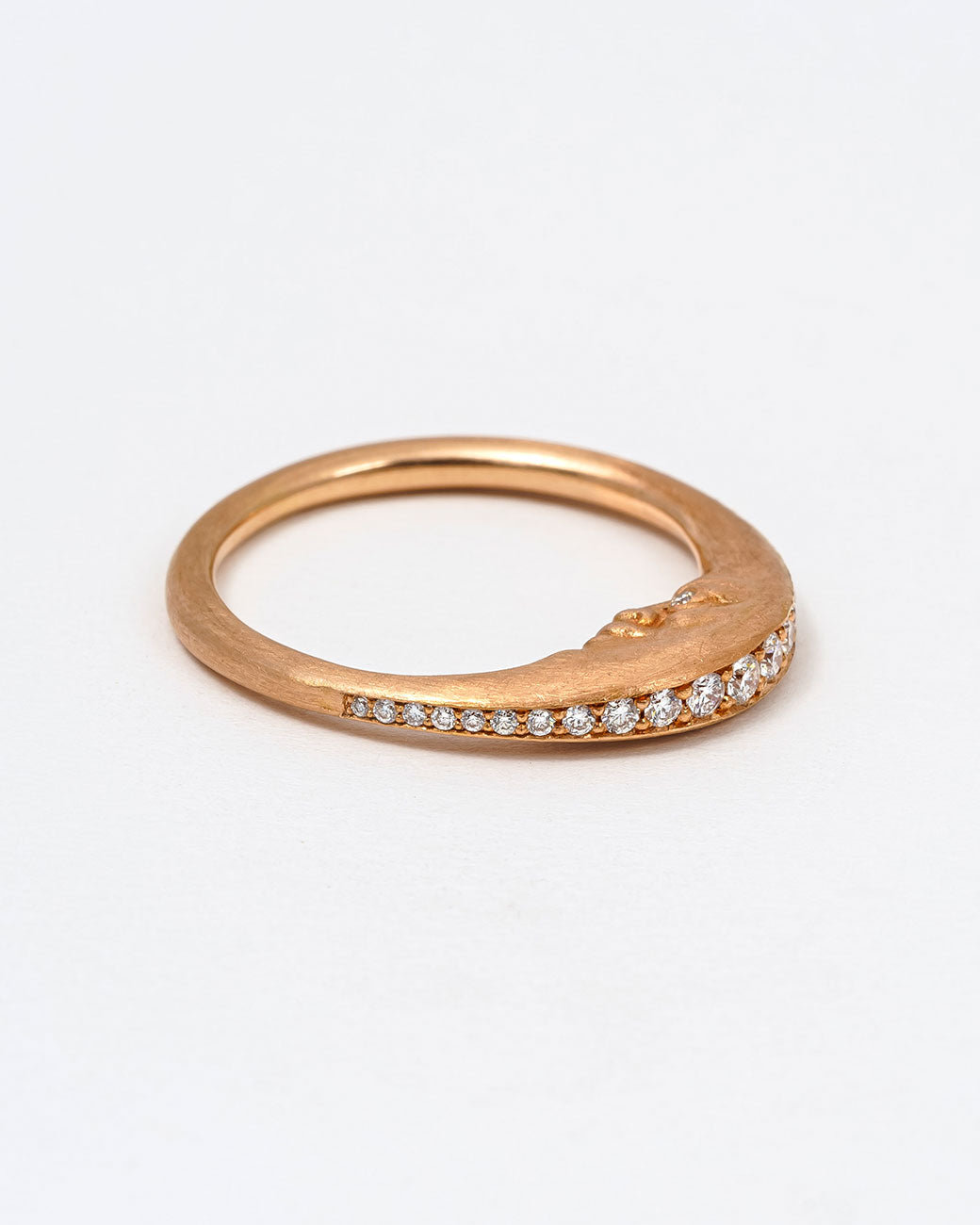 A rose gold crescent moon ring with a diamond eyed face and graduated white diamonds around the top edge. Shown lying flat from the bottom.