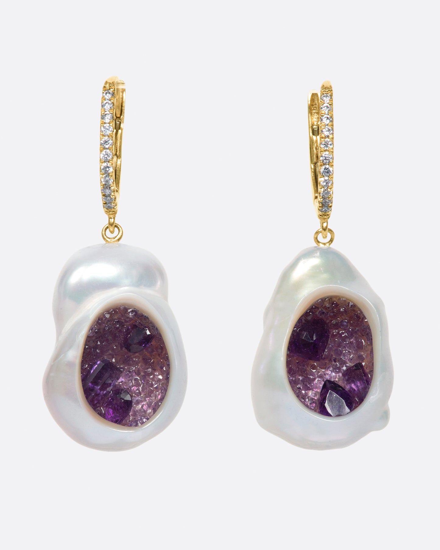 A pair of dangle earrings with carved out pearls lined with amethysts. Each earring is topped with yellow gold ear hook with pave diamonds. Shown from the front.