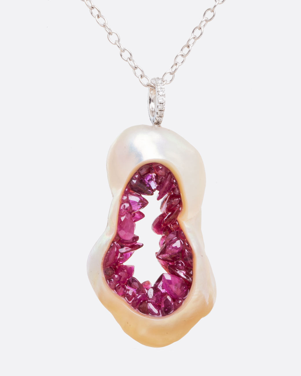Close up straight on view of hollowed out souffle pearl with interior lined with shards of ruby with a pave diamond bail connecting the pendant to a white gold chain.