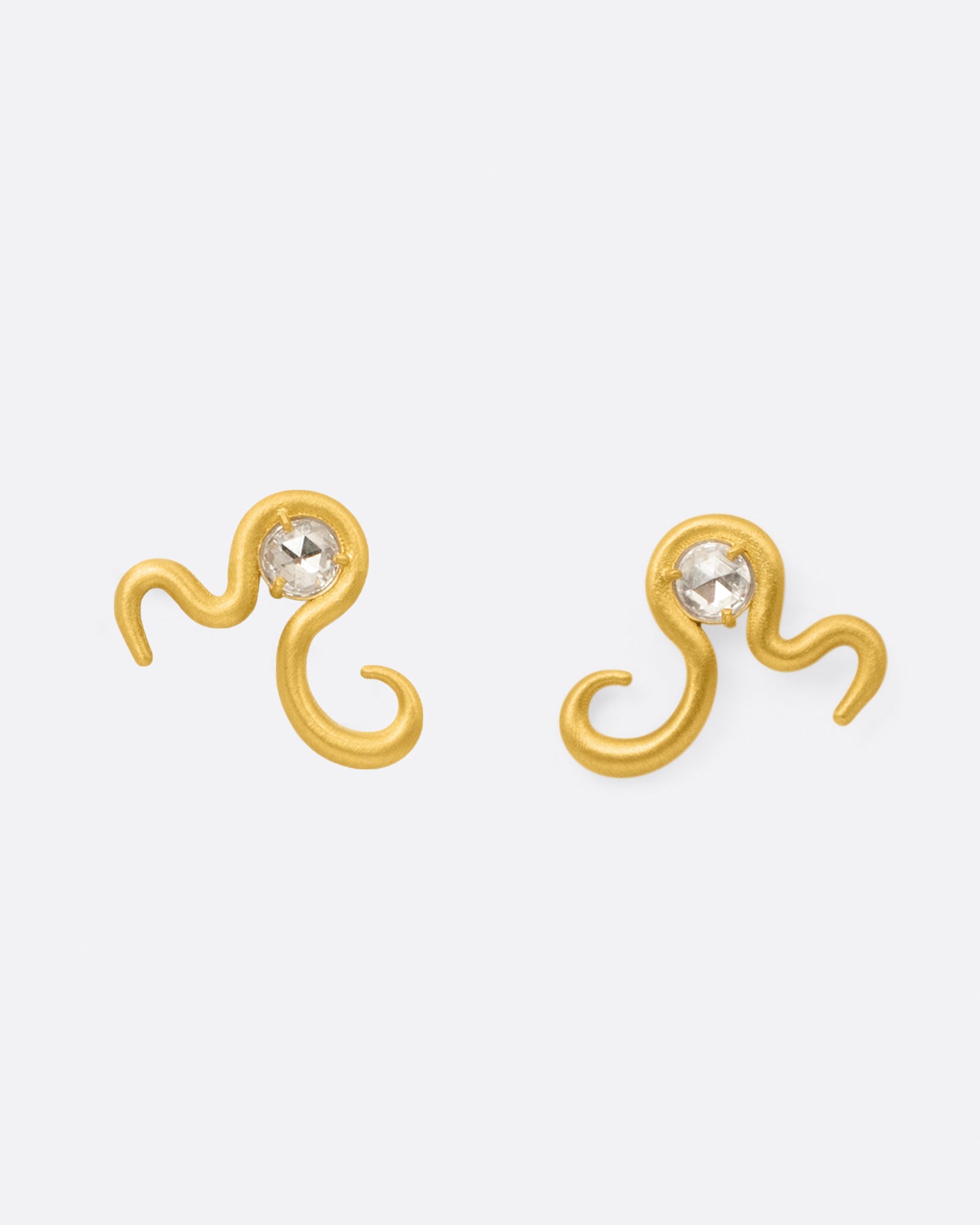 A pair of high karat yellow gold curved snake stud earrings with a rose cut diamond at their centers, shown from the front.