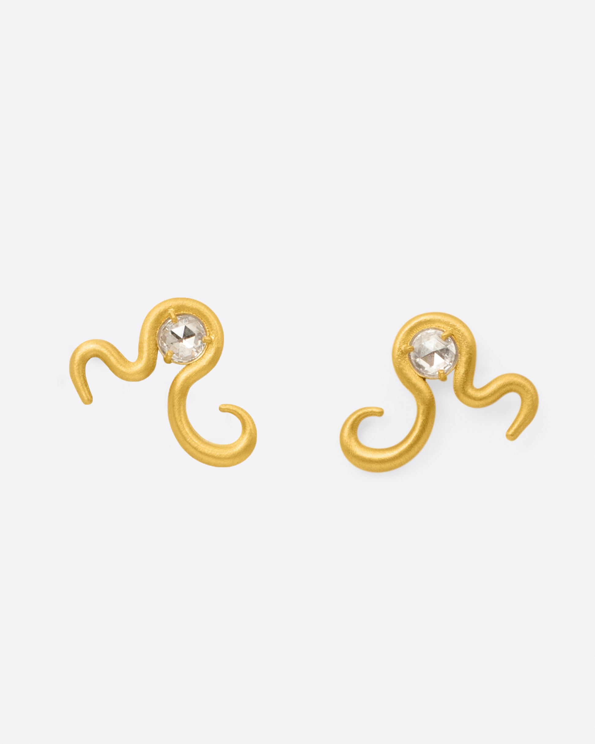 A pair of high karat yellow gold curved snake stud earrings with a rose cut diamond at their centers, shown from the front.