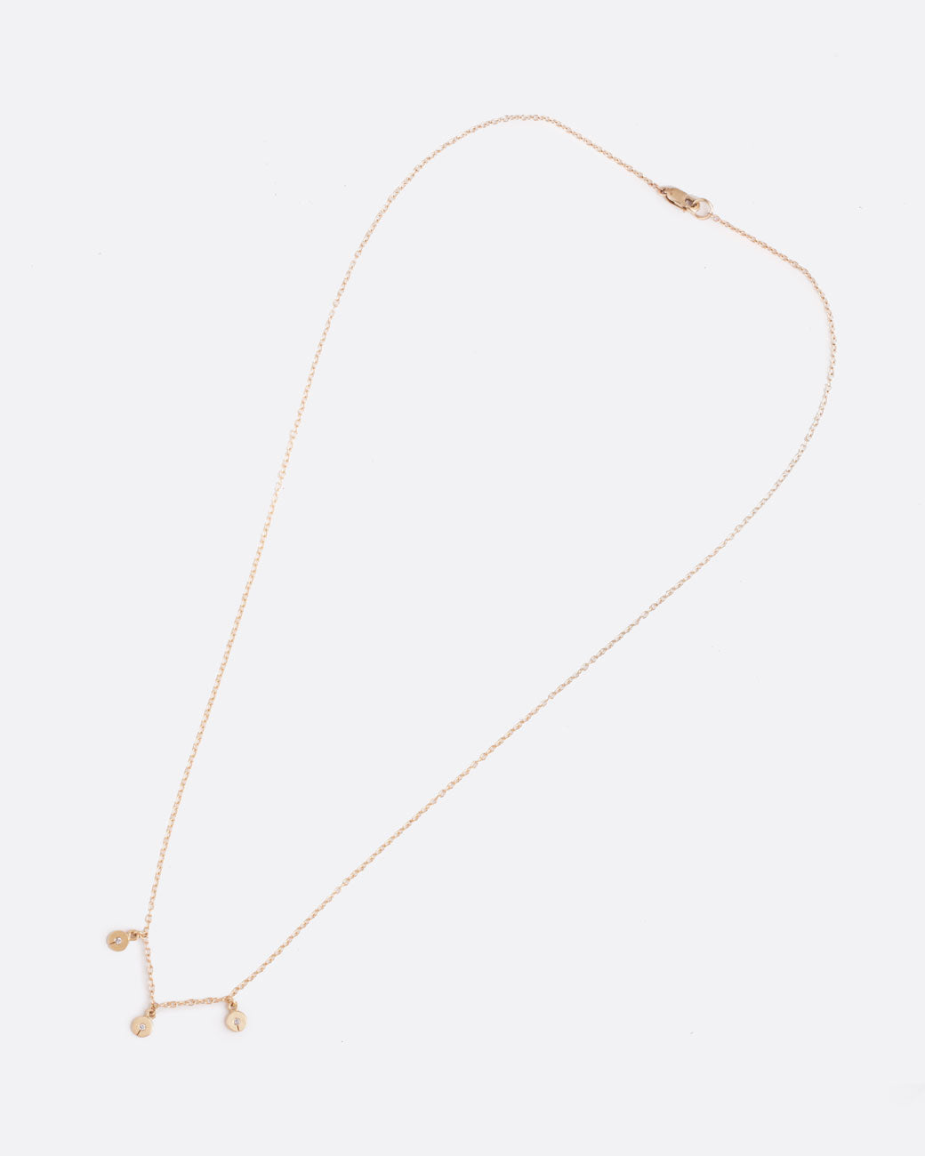 A yellow gold cable chain necklace with three disc charms. Each disc has a single gray diamond with a slit in the bottom. Shown clasped diagonally from the front.