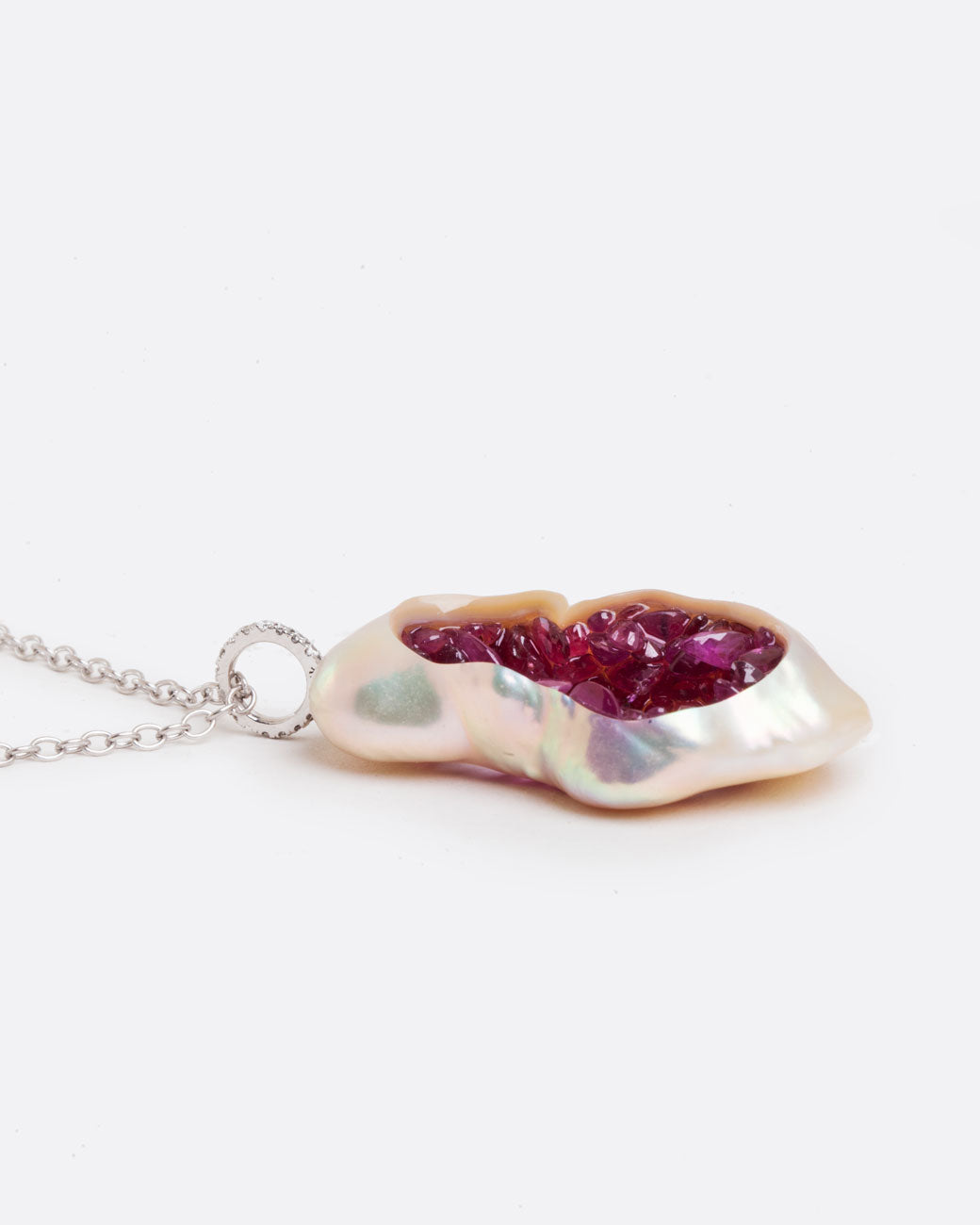 Close up side view of hollowed out souffle pearl with interior lined with shards of ruby with a pave diamond bail connecting the pendant to a white gold chain.