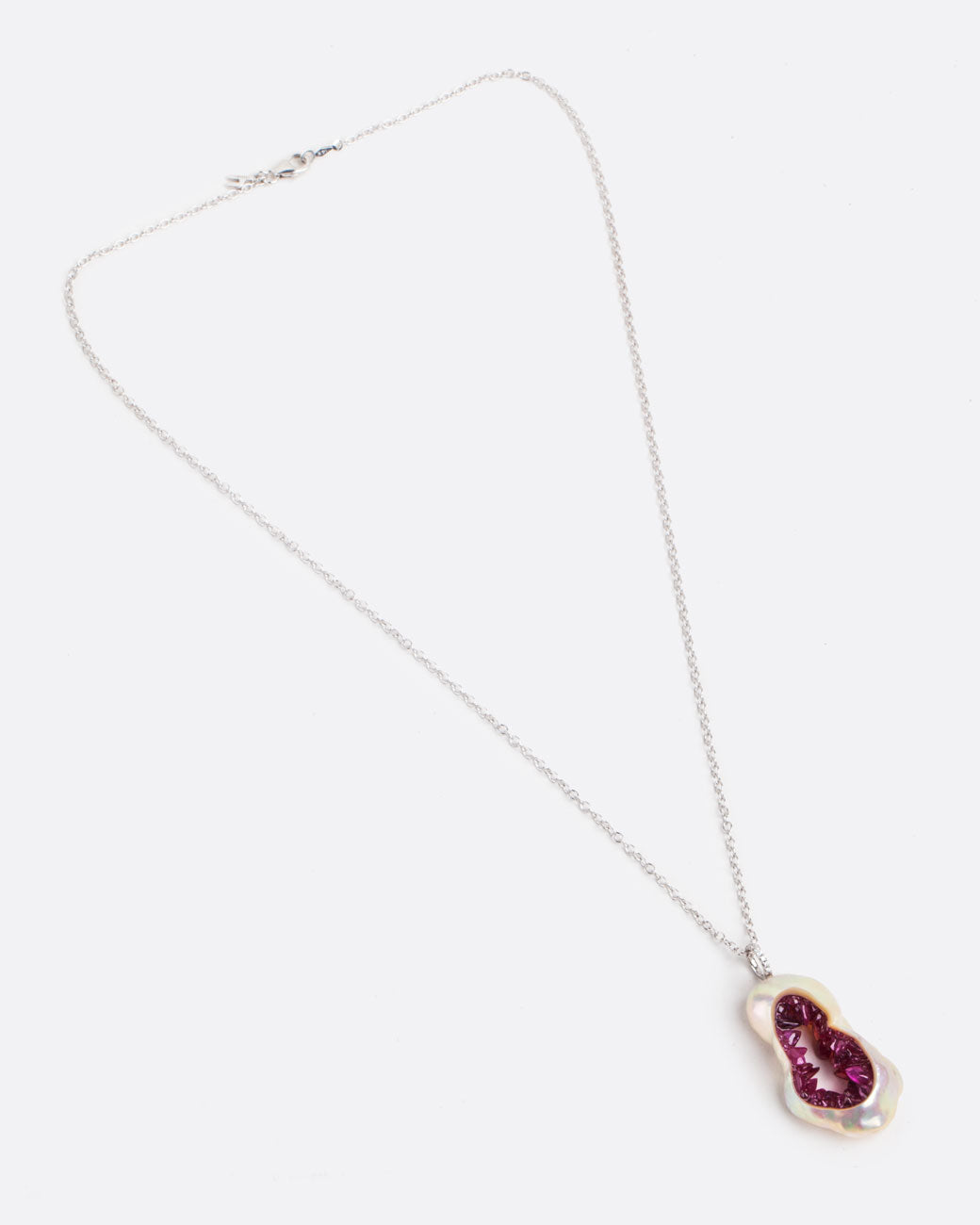 Layflat view of hollowed out souffle pearl with interior lined with shards of ruby with a pave diamond bail connecting the pendant to a white gold chain. 