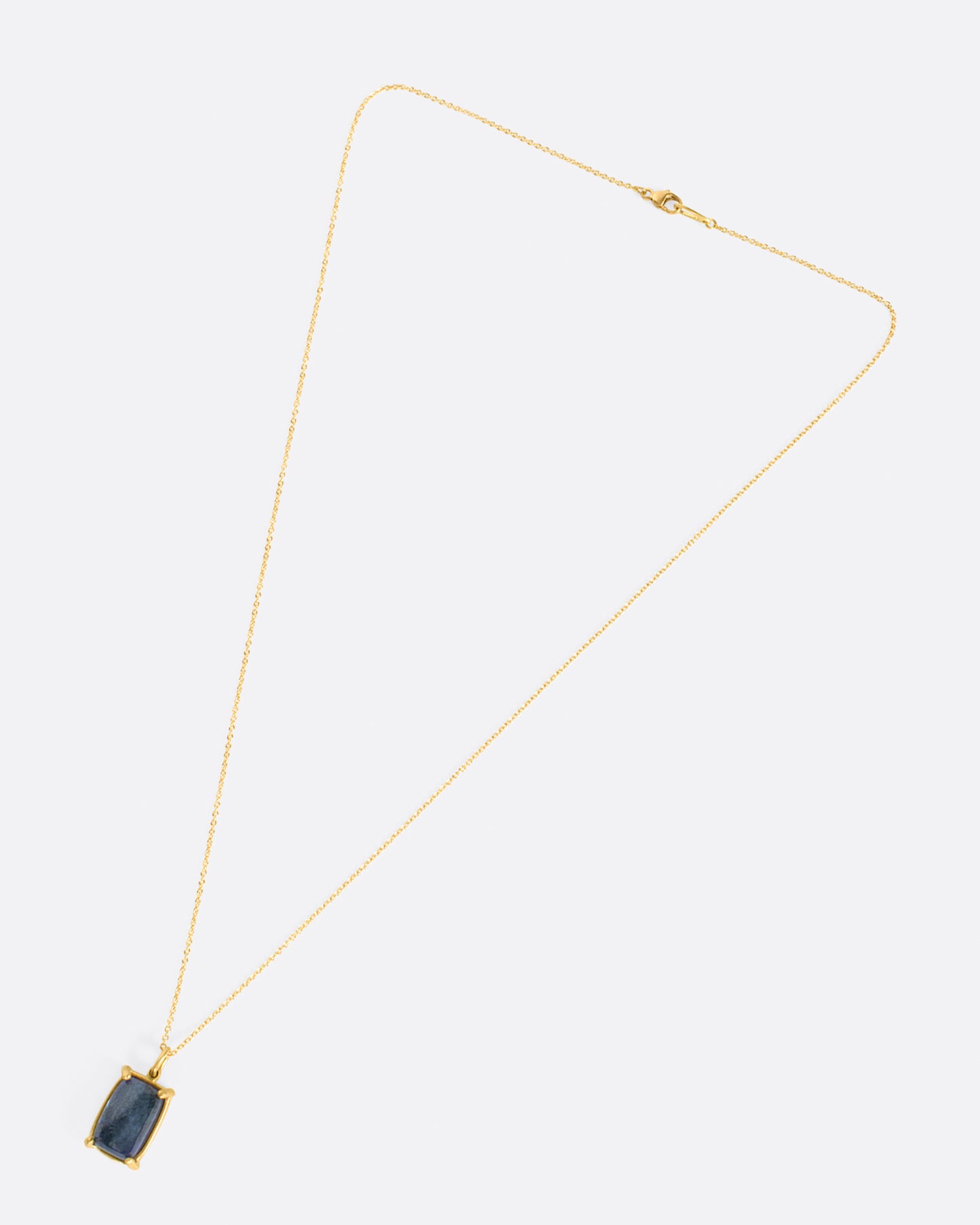 A large, rectangular tanzanite cabochon pendant set in matte gold prongs on a cable chain necklace.