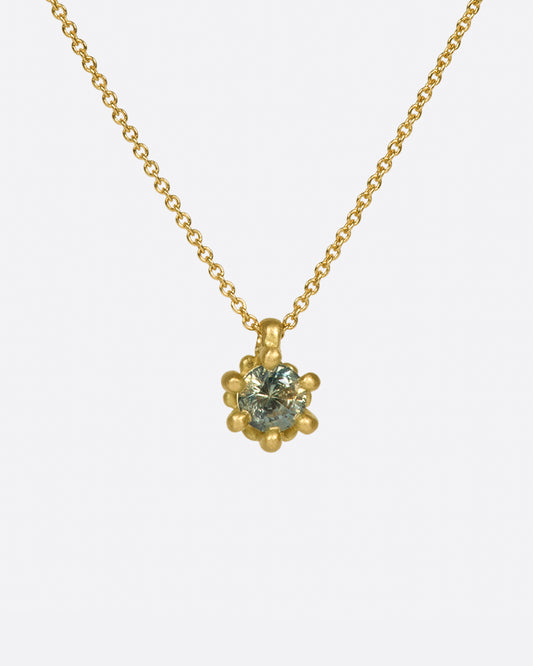 A two-tone green sapphire pendant set in a flowery gold setting on a classic cable chain necklace.