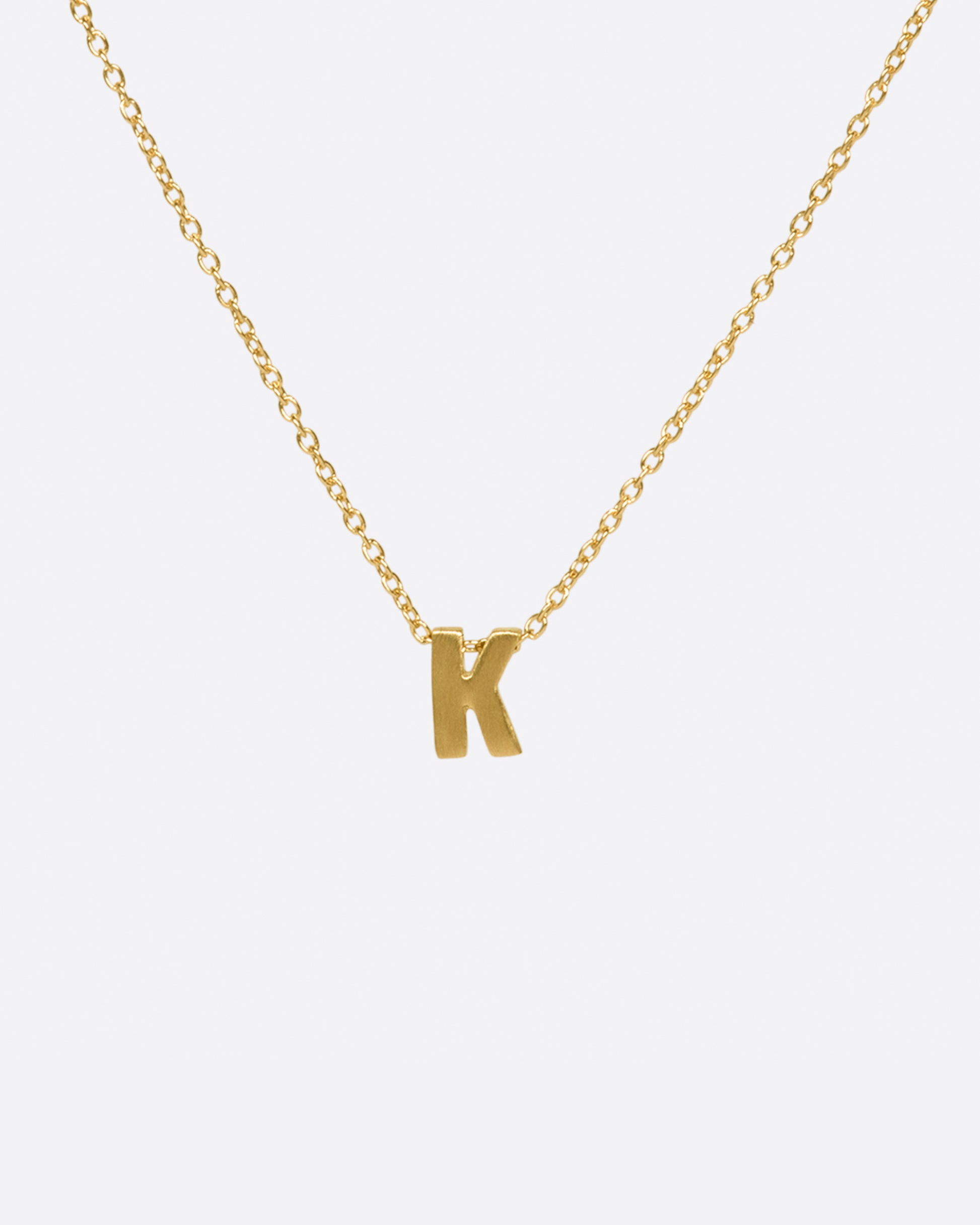 A yellow gold cable chain necklace with a letter K initial pendant. Shown from the front.