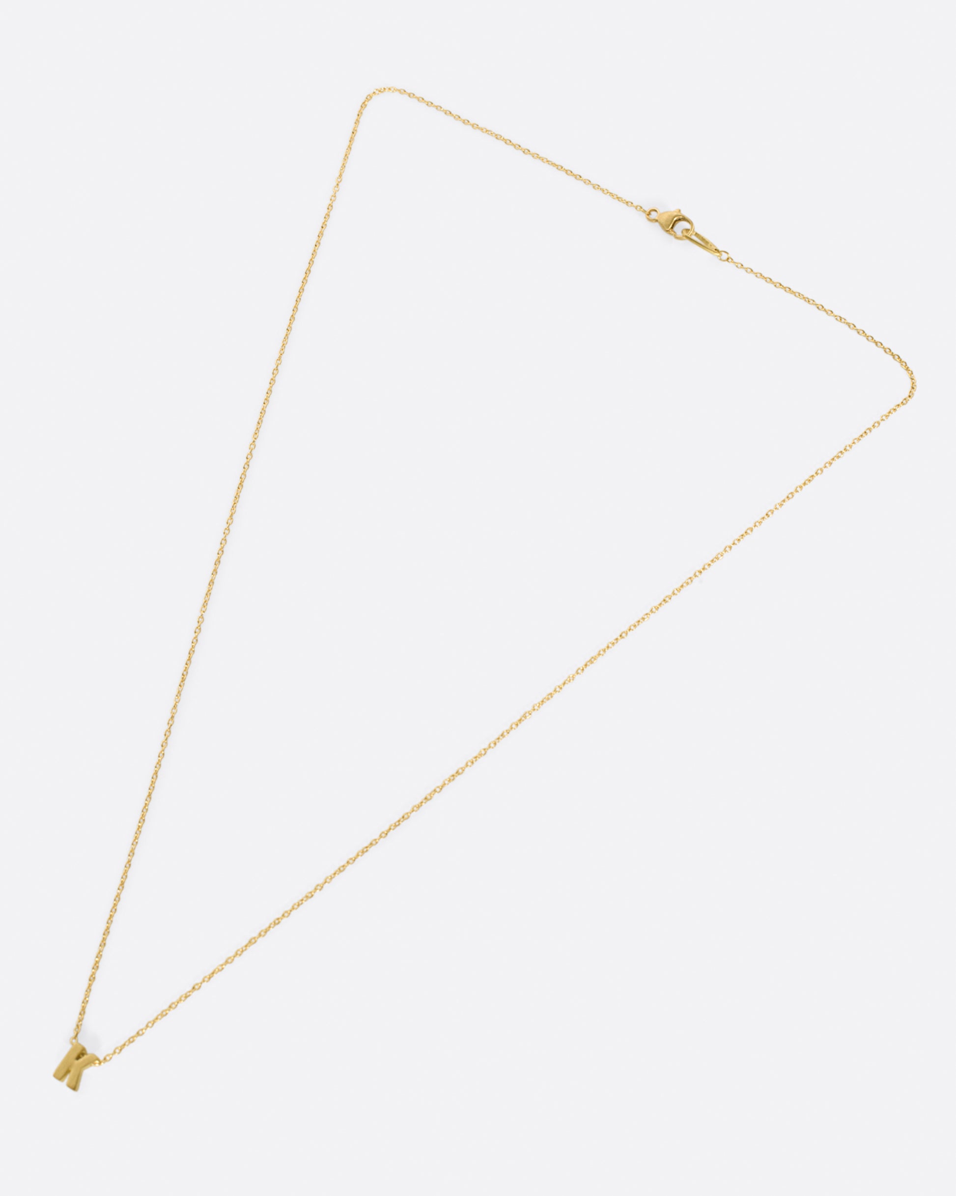 A yellow gold cable chain necklace with a letter K initial pendant. Shown from the front.