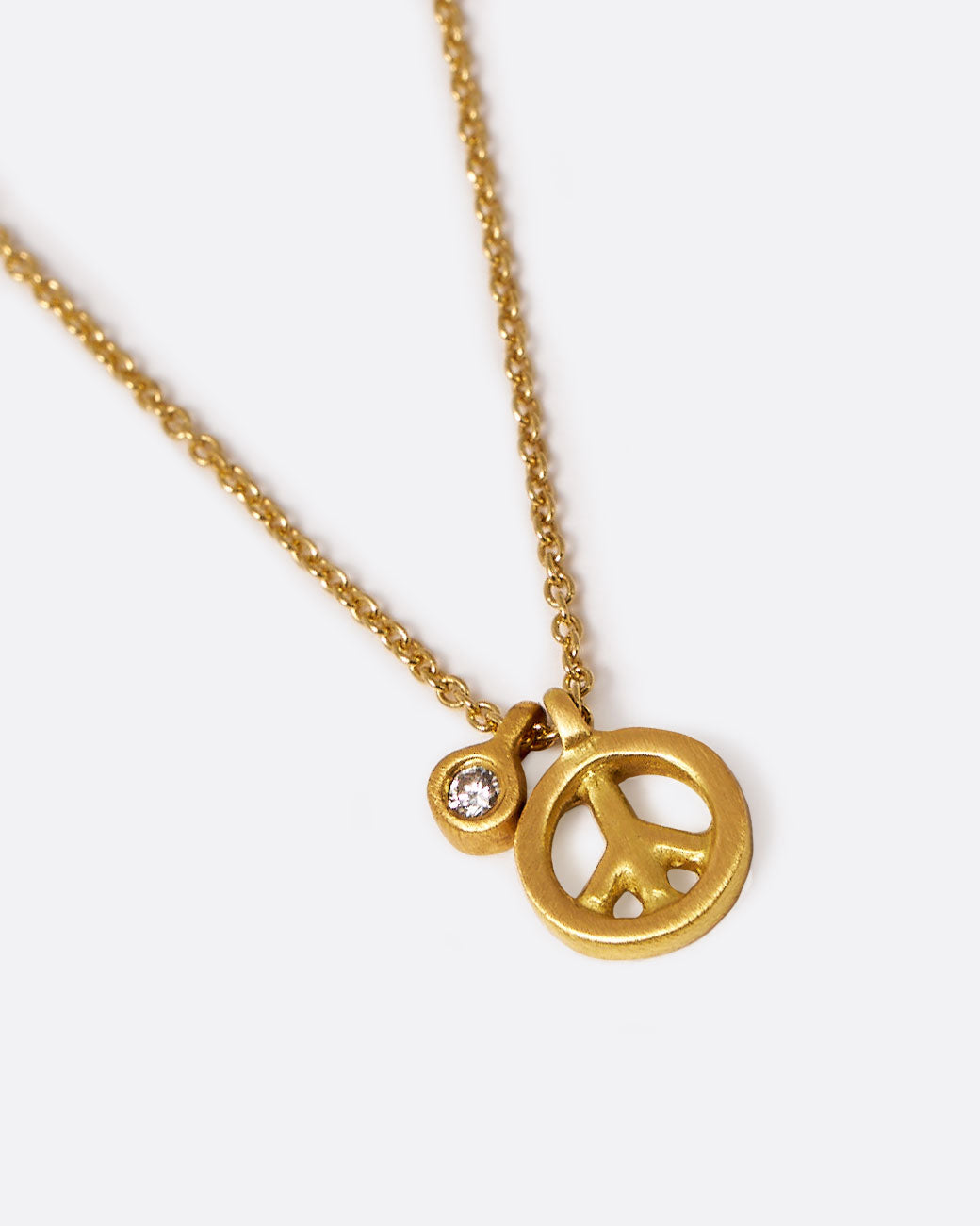 A yellow gold cable chain necklace with a peace sign pendant and a bezel set diamond tag. Shown lying flat from the front.