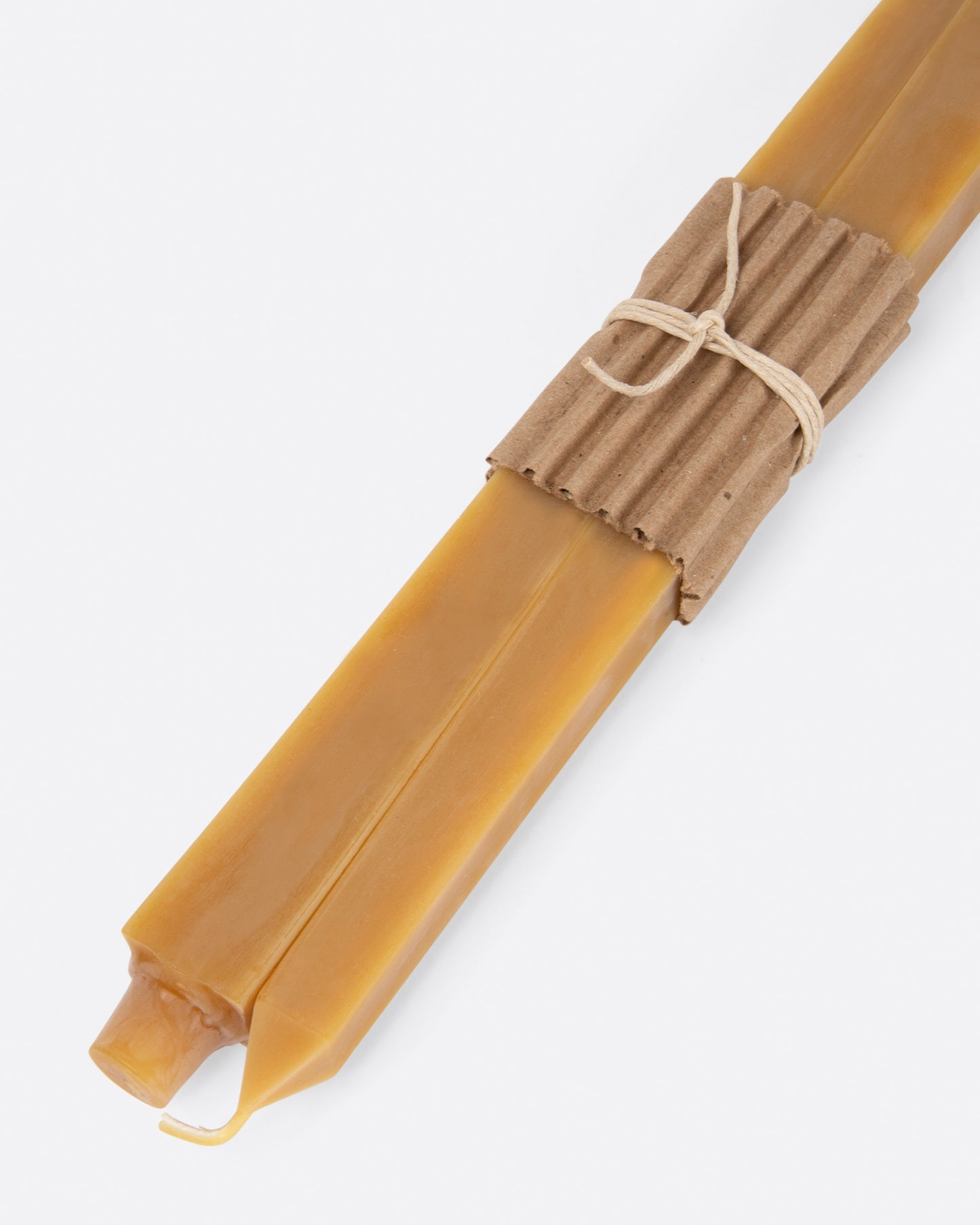 Gold square taper candles lying flat at an angle with cardboard wrapping at the center.
