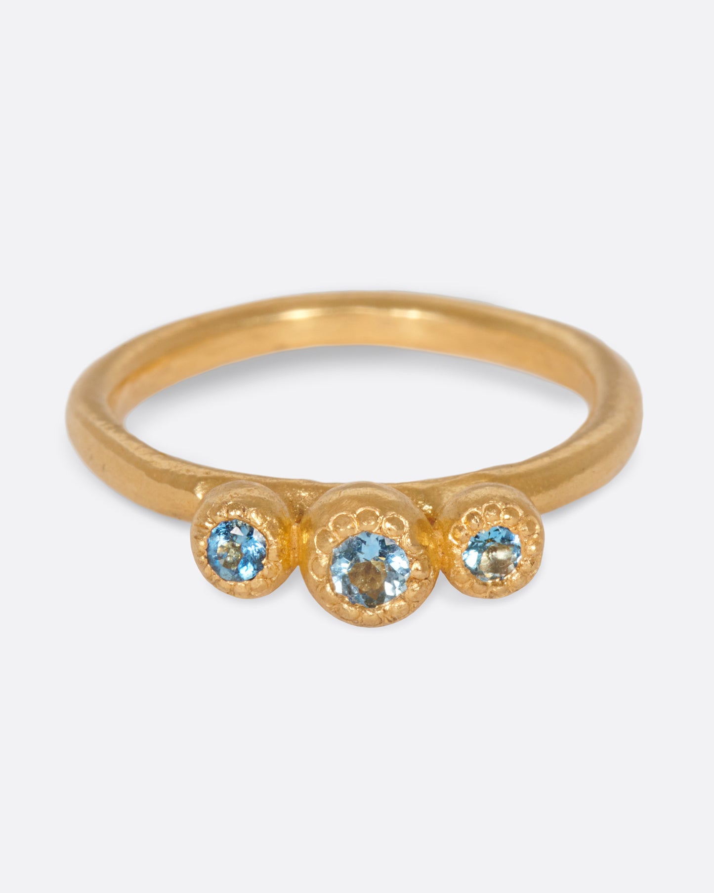 A handmade, high karat gold ring with three vibrant, bezel set aquamarines.