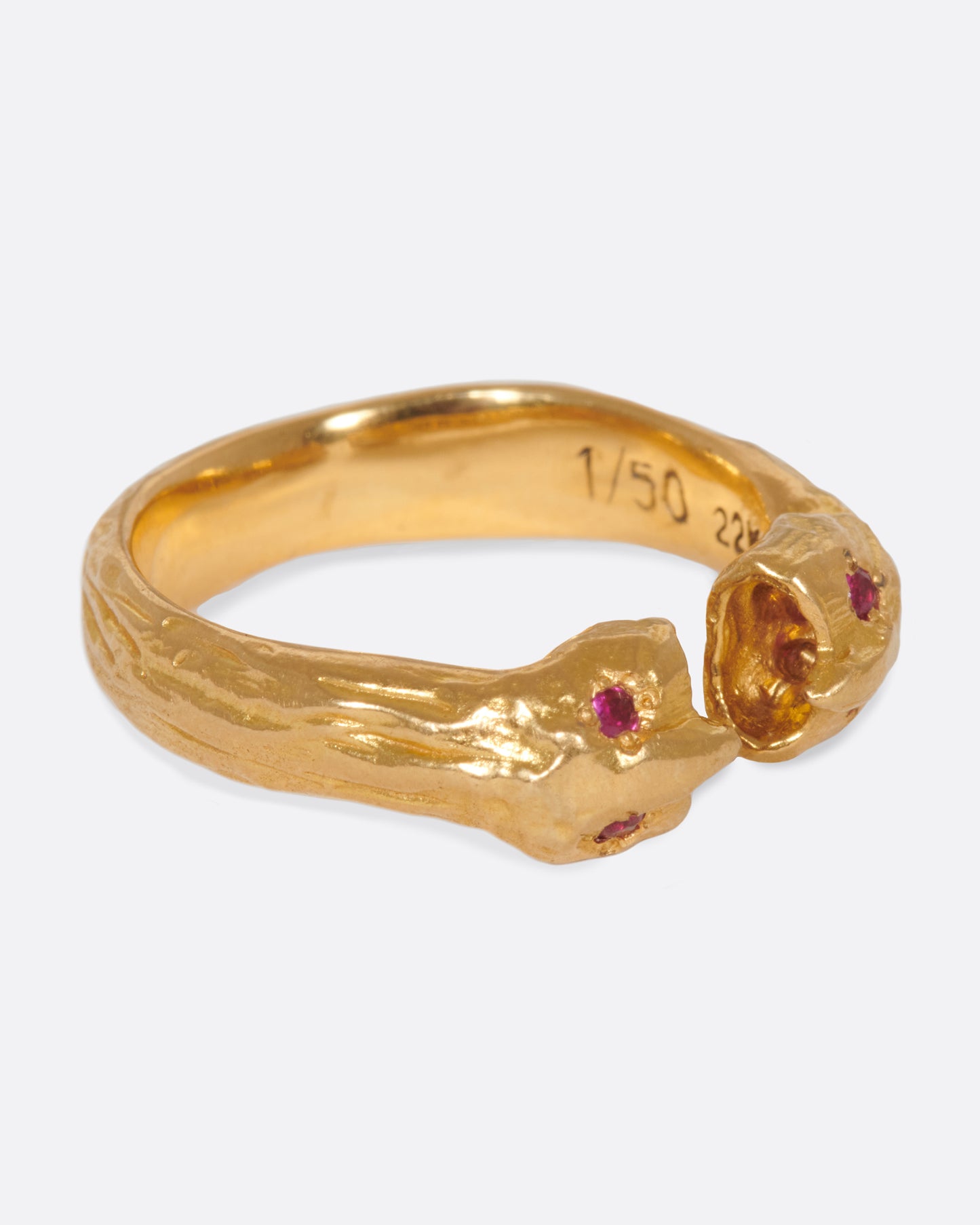 A yellow gold open ring with two ruby eyed faces facing each other. Shown from the side.