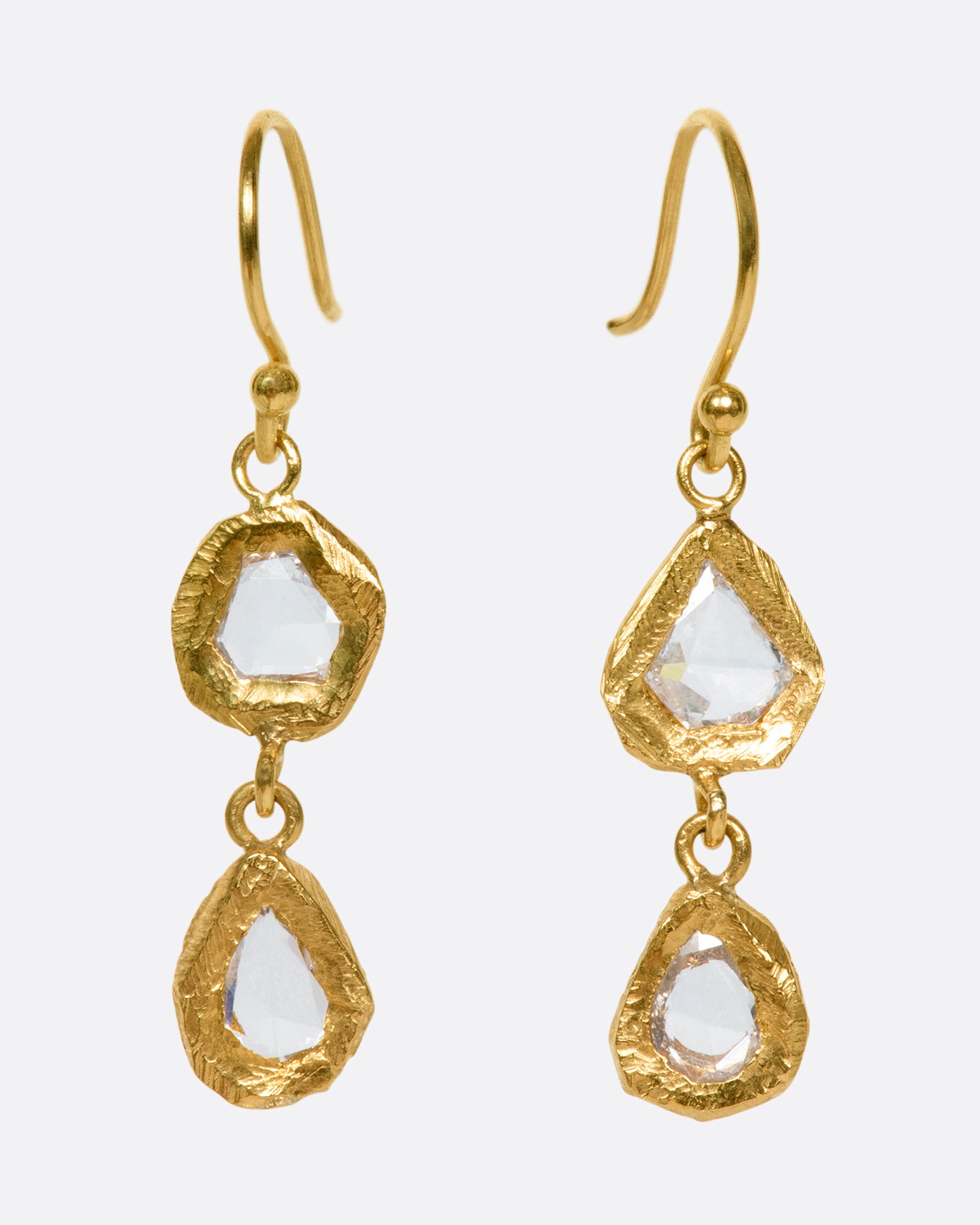 A pair of slightly asymmetrical yellow gold diamond drop earrings with two diamonds set in hand carved bezels on each earring. Shown from the front.