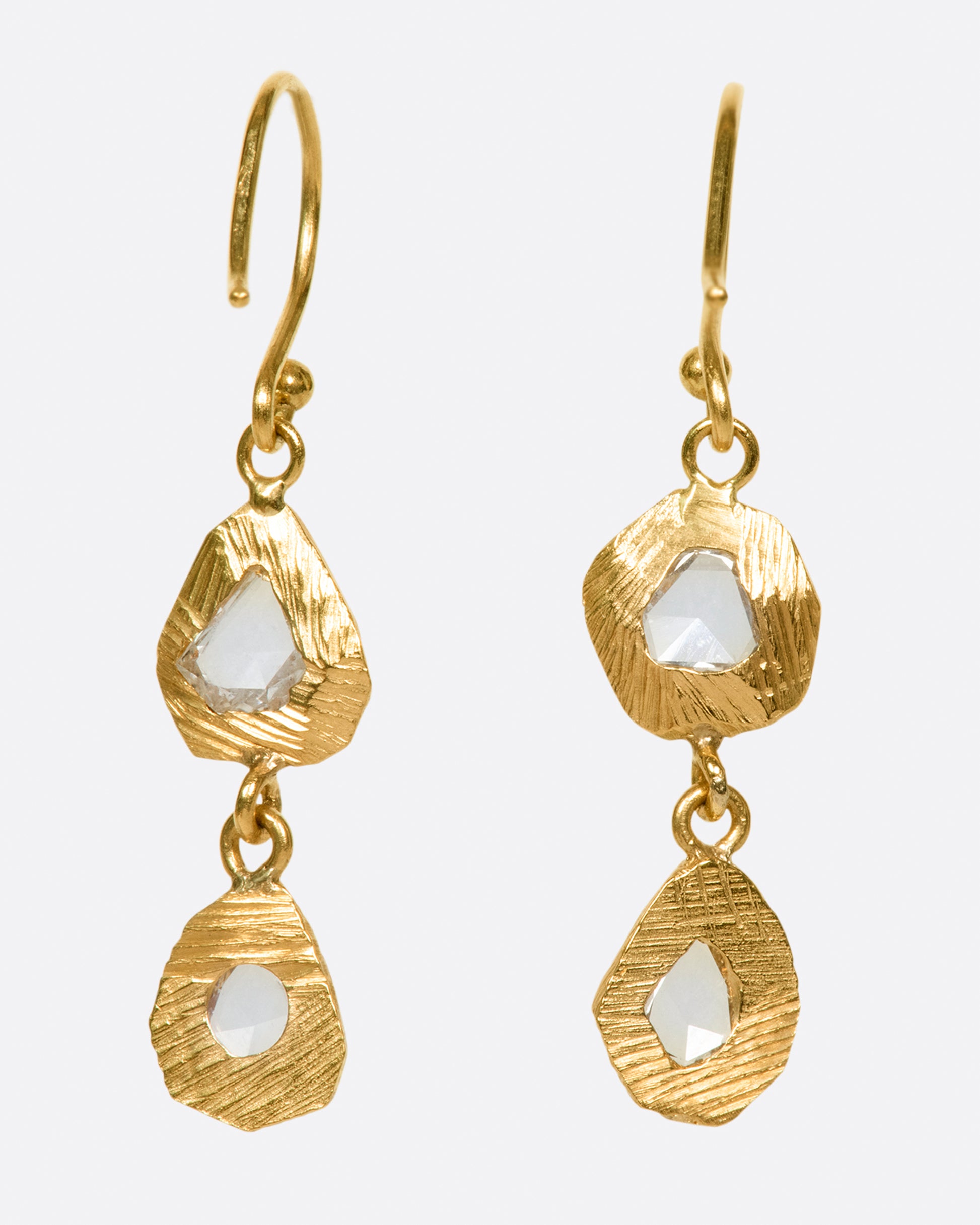 A pair of slightly asymmetrical yellow gold diamond drop earrings with two diamonds set in hand carved bezels on each earring. Shown from the back.