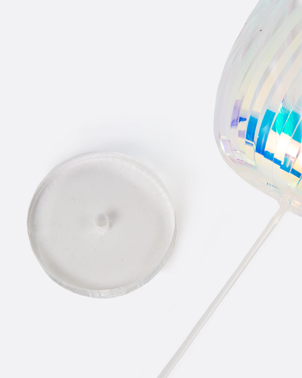 A close up of plastic disc shaped rainbow stick holder. An iridescent rainbow stick is lying flat in the corn