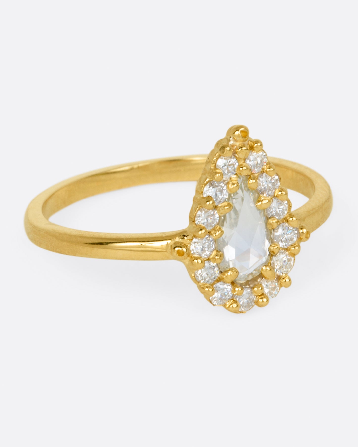 A yellow gold ring with a light champagne rose cut pear shaped diamond haloed by round diamonds. Shown from the side.