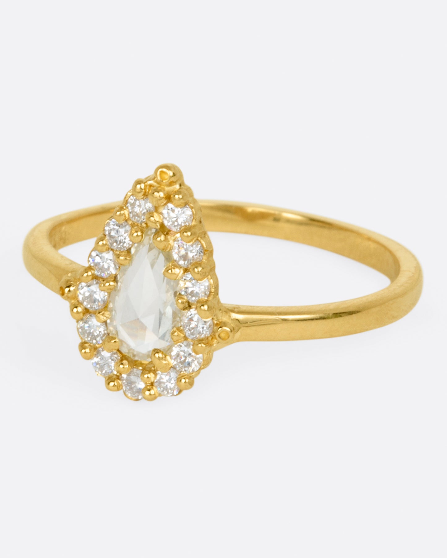 A yellow gold ring with a light champagne rose cut pear shaped diamond haloed by round diamonds. Shown from the side.