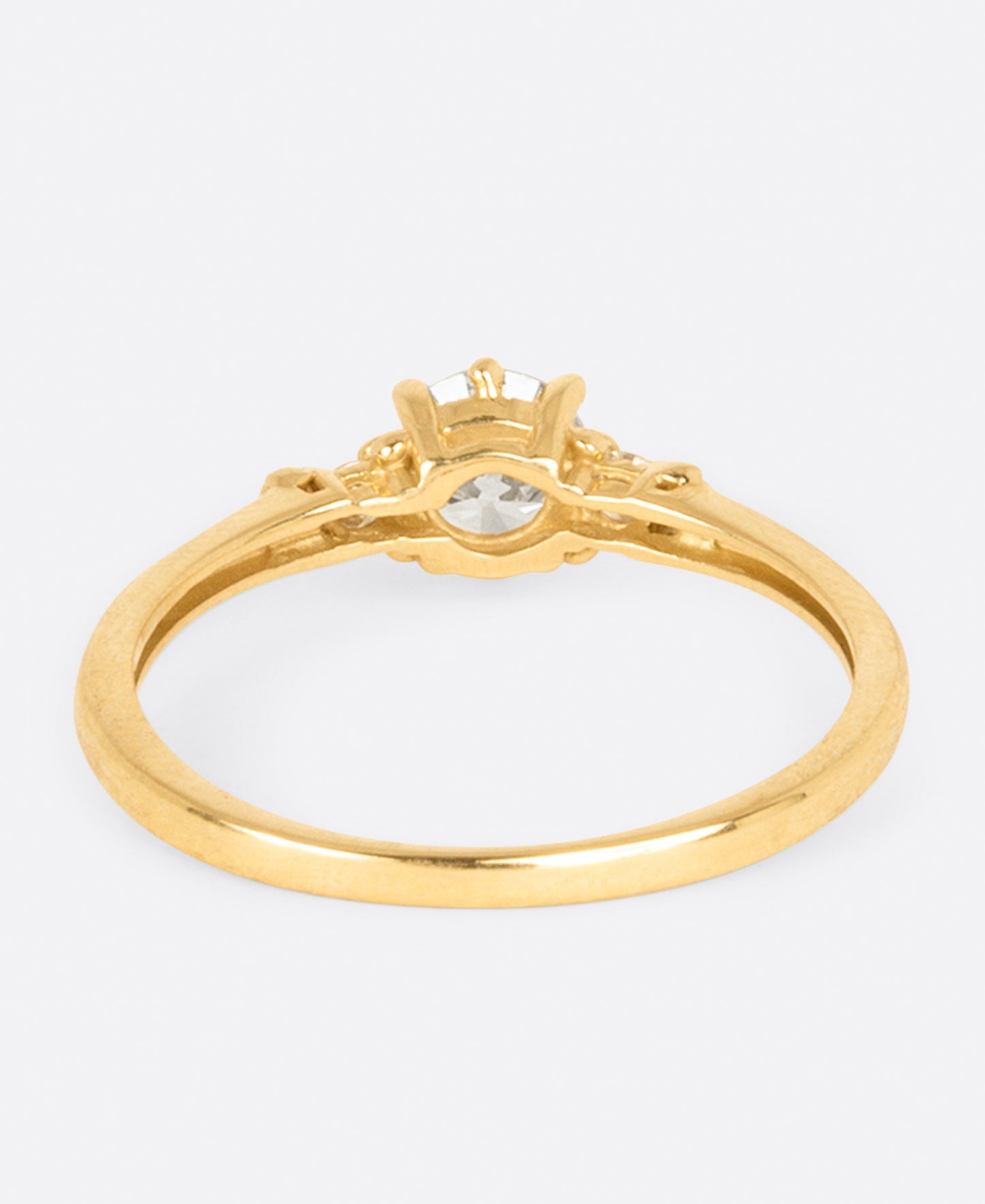 A yellow gold diamond ring with one large round central diamond and two smaller round diamonds on either side. Shown from the back.