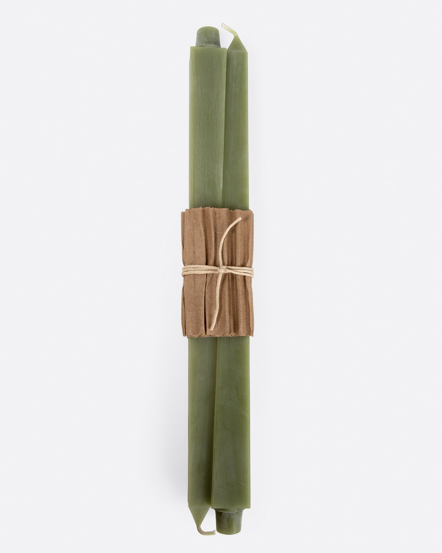 Sage green square taper candles lying flat with cardboard wrapping at the center. Shown from the front.