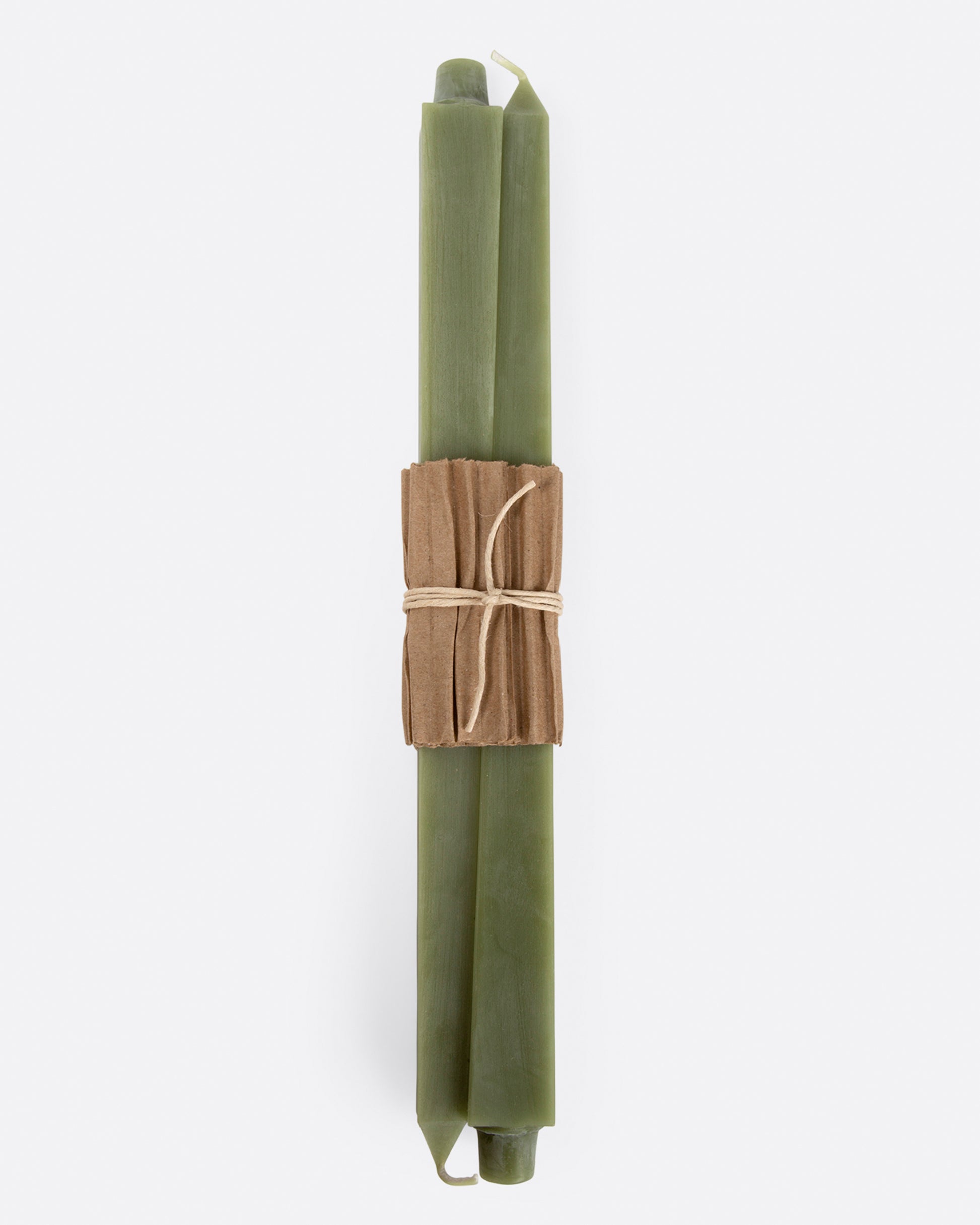 Sage green square taper candles lying flat with cardboard wrapping at the center. Shown from the front.
