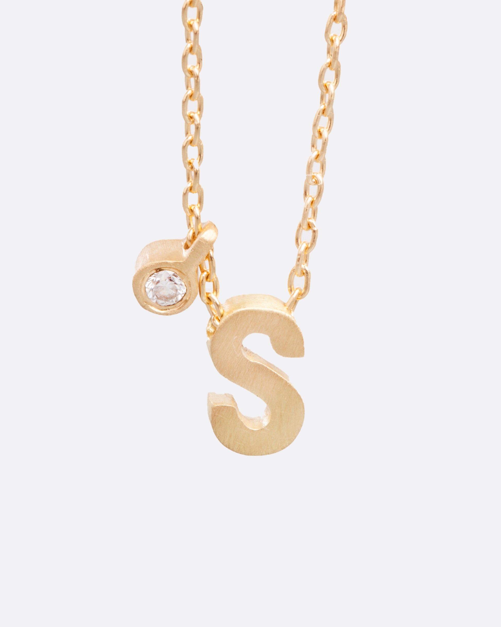 A yellow gold cable chain necklace with a letter S initial pendant. Shown from the front with a separate bezel set diamond tag.