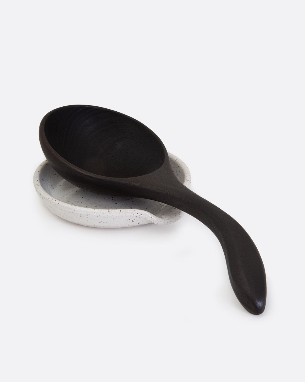 A white stoneware spoon rest shown with a black wooden spoon resting on it. Shown at an angle.