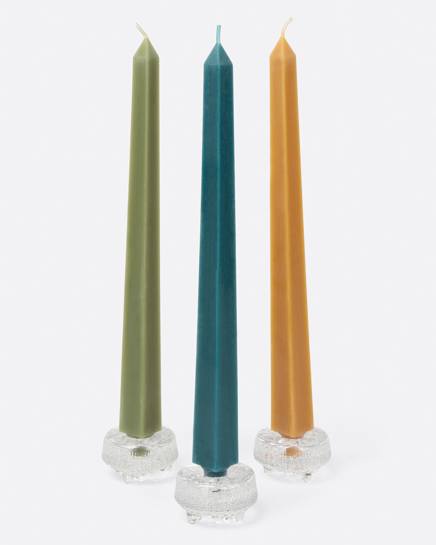Three square taper candles, (one green, one turquoise, one gold) in glass candle holders. Shown from the front.