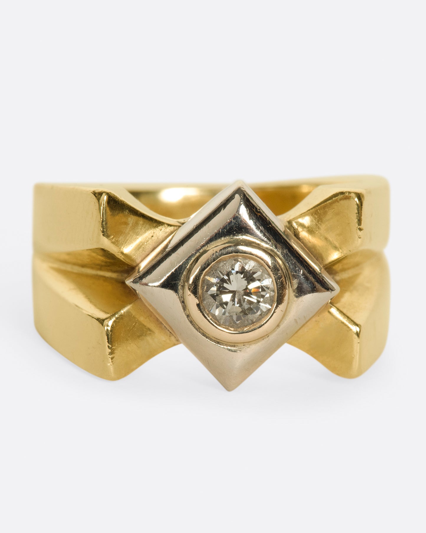 A heavy, gold, X-shaped ring with a white gold square and a round diamond at its center. Shown from the front.