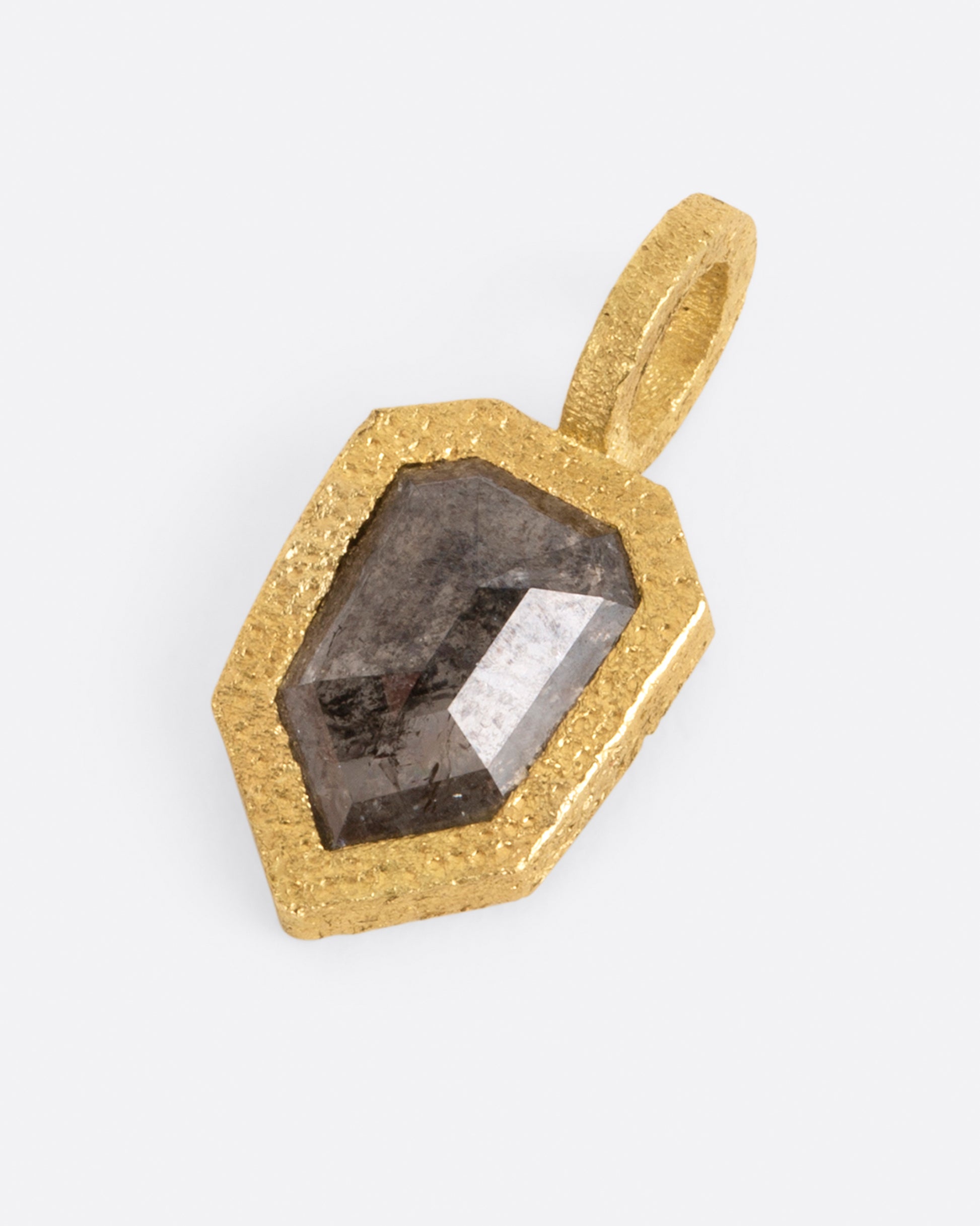 A pendant with a shield shaped salt and pepper diamond set in yellow gold. Shown lying flat from the front.