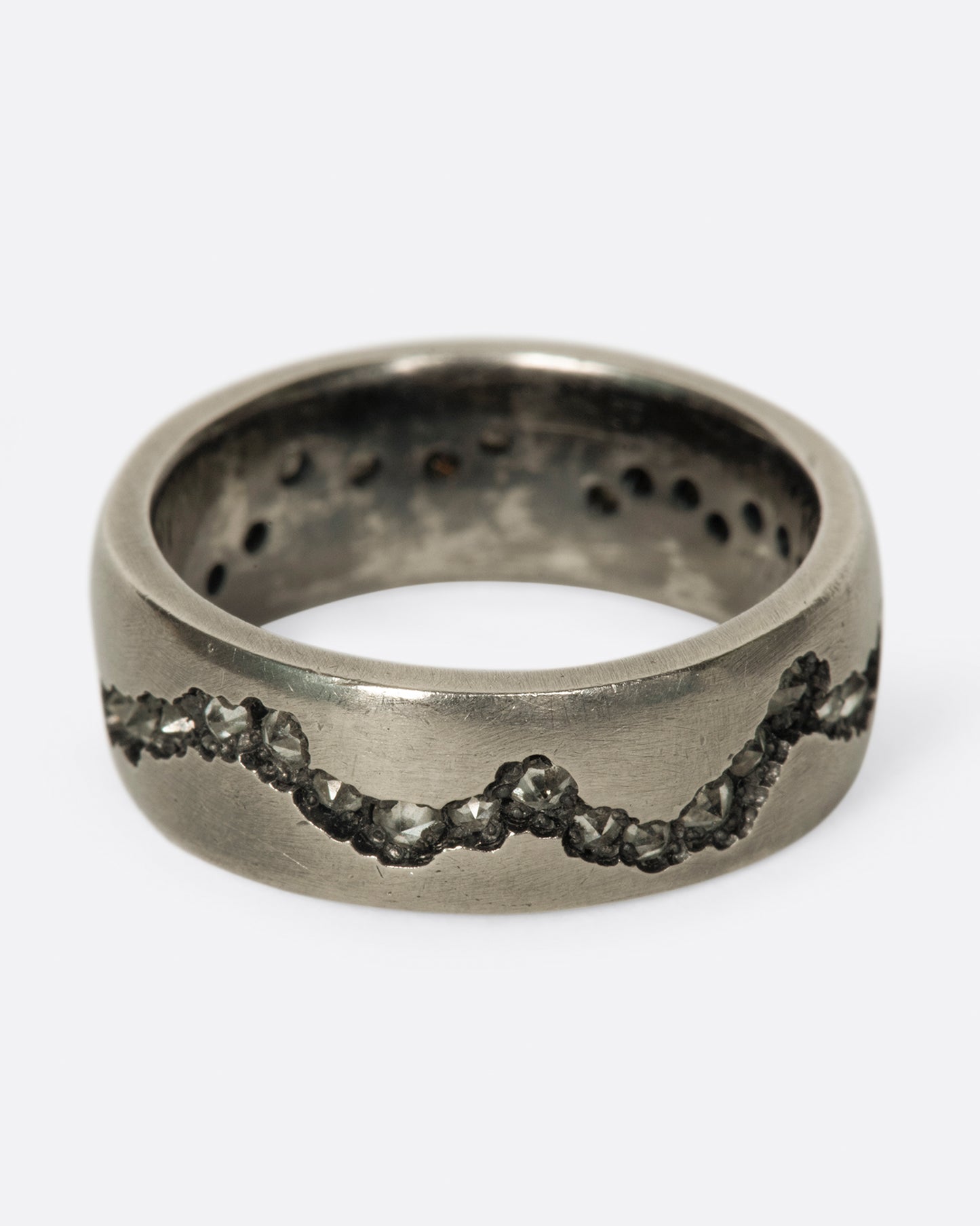 A wide palladium band with inverted diamonds set in a hand cut fissure through the center of the ring. Shown from the front.