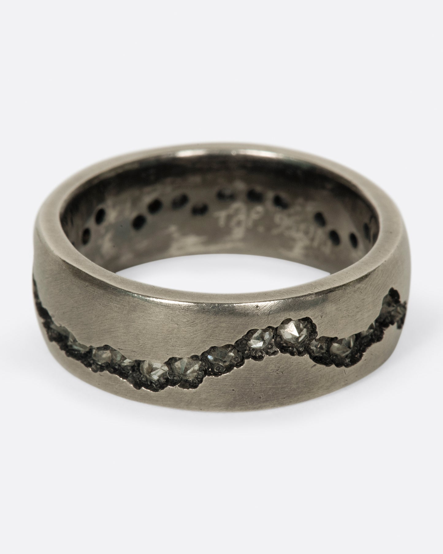A wide palladium band with inverted diamonds set in a hand cut fissure through the center of the ring. Shown from the front.
