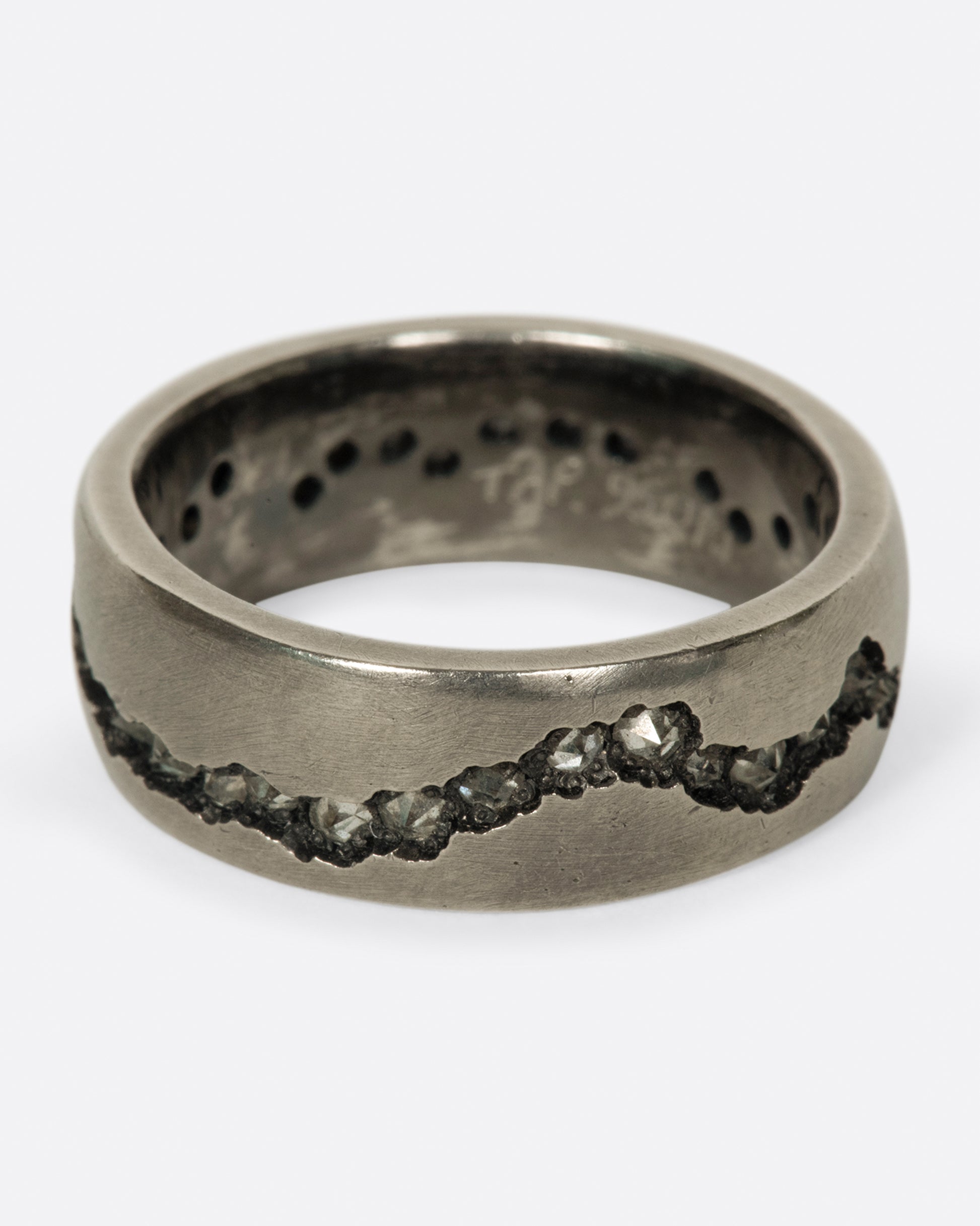 A wide palladium band with inverted diamonds set in a hand cut fissure through the center of the ring. Shown from the front.
