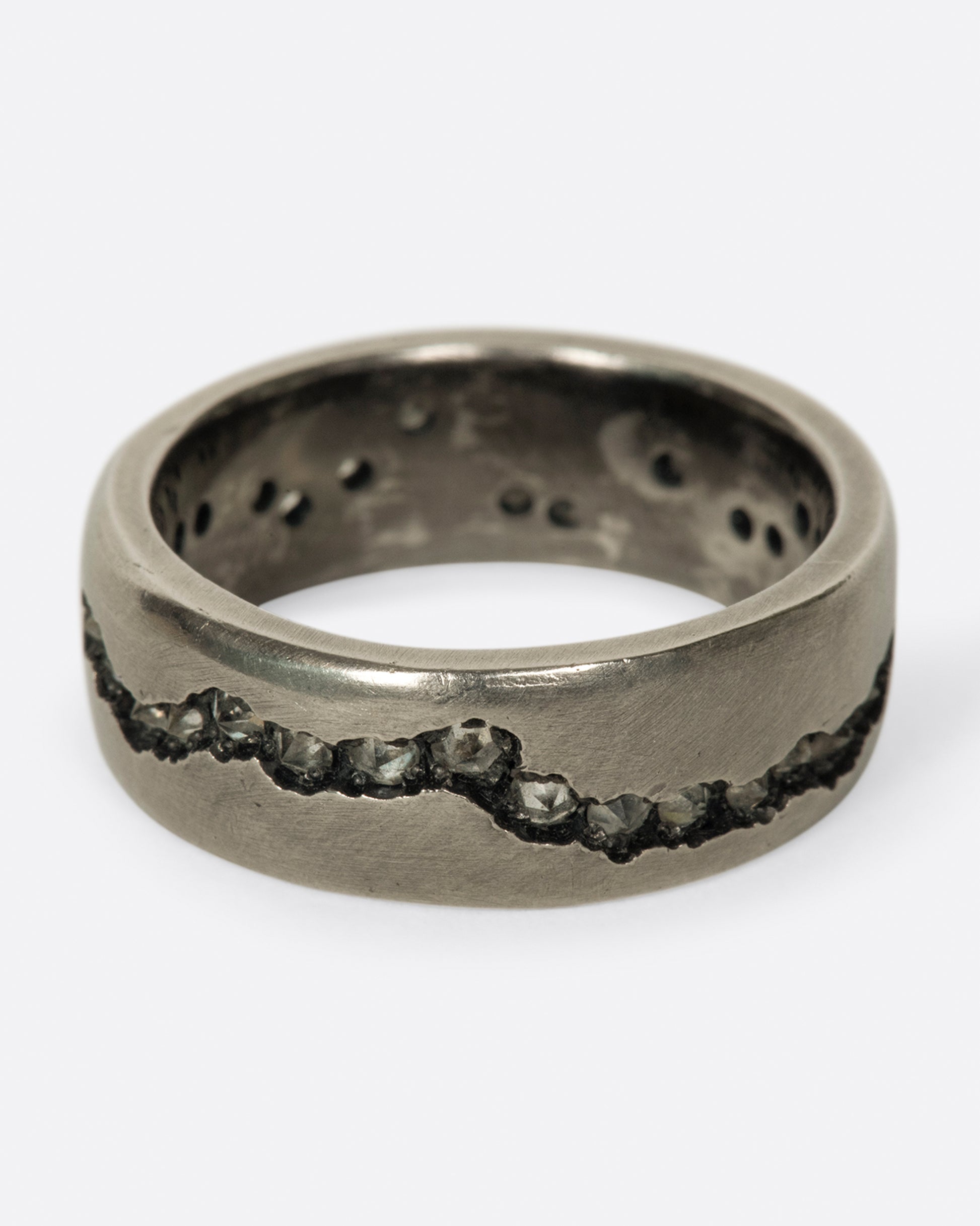 A wide palladium band with inverted diamonds set in a hand cut fissure through the center of the ring. Shown from the front.