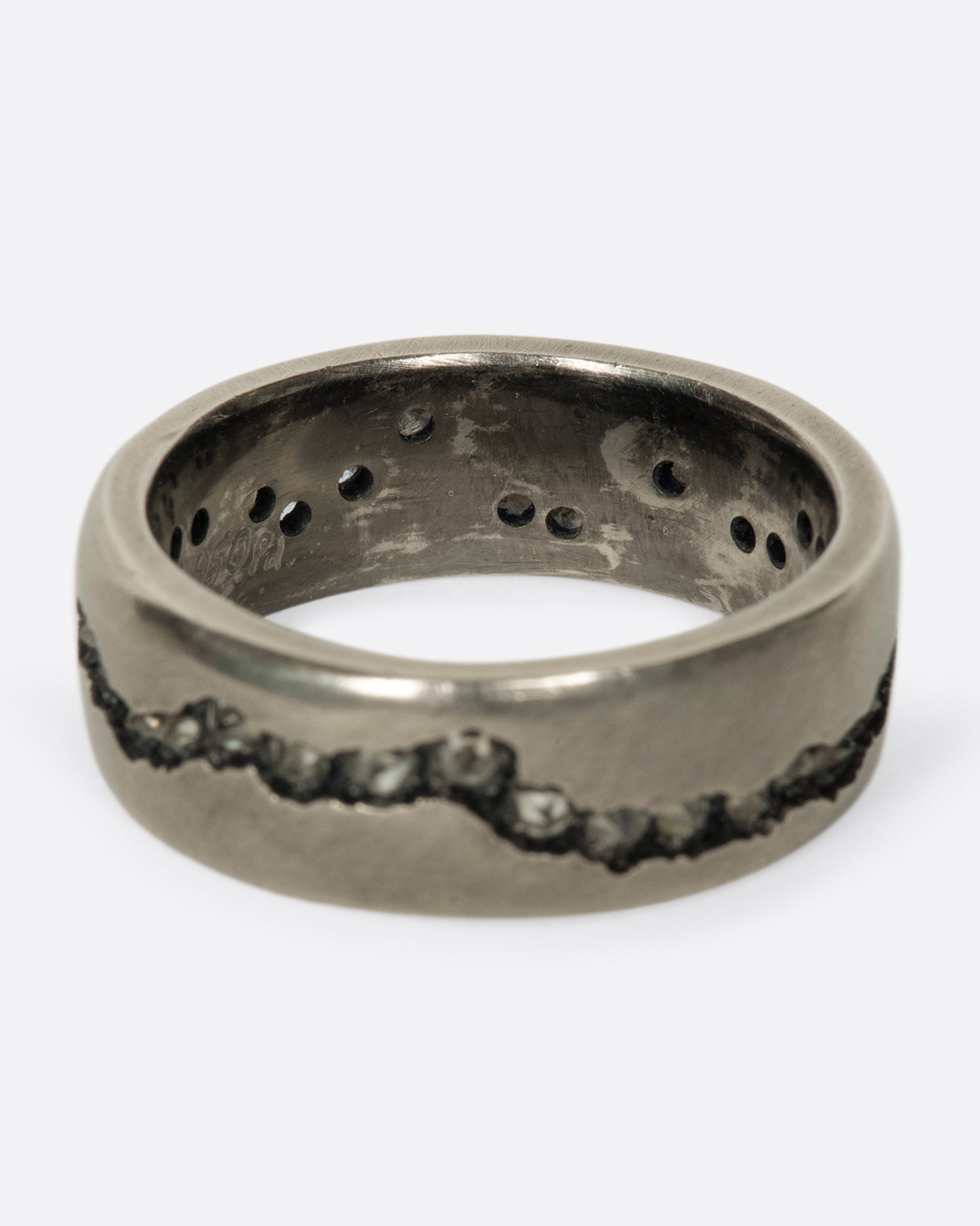 A wide palladium band with inverted diamonds set in a hand cut fissure through the center of the ring. Shown from the back.