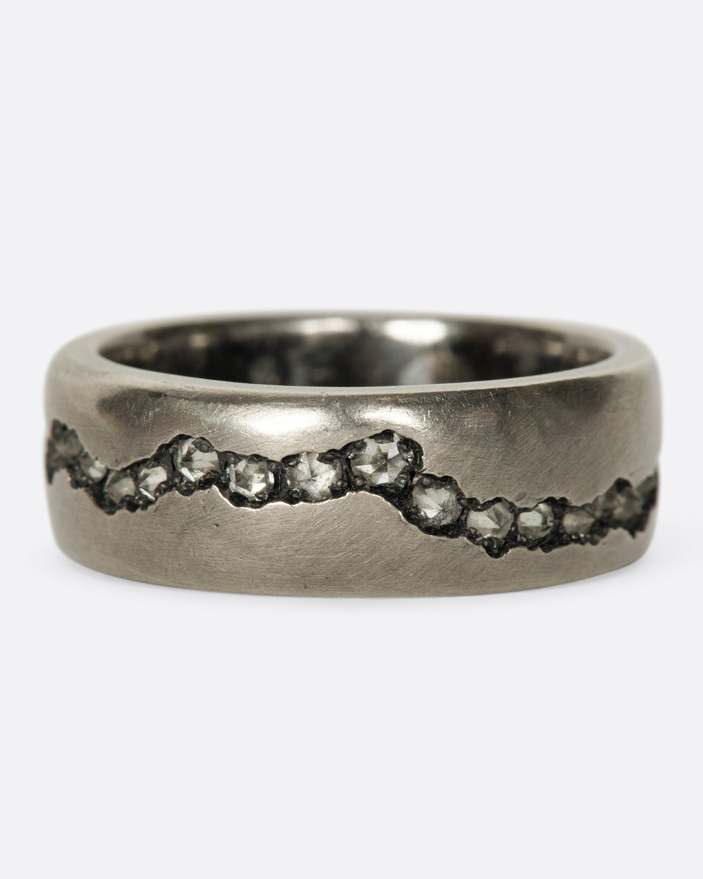 A wide palladium band with inverted diamonds set in a hand cut fissure through the center of the ring. Shown from the front.