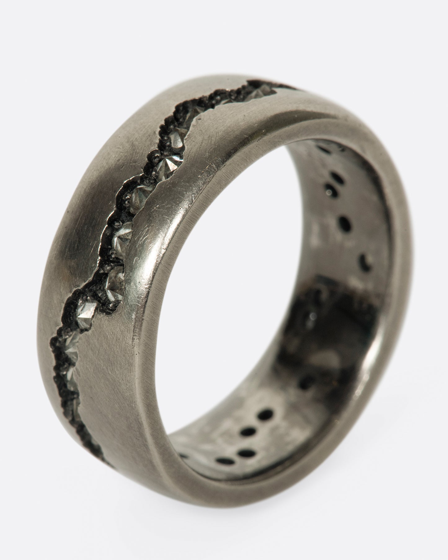 A wide palladium band with inverted diamonds set in a hand cut fissure through the center of the ring. Shown standing up from the side.