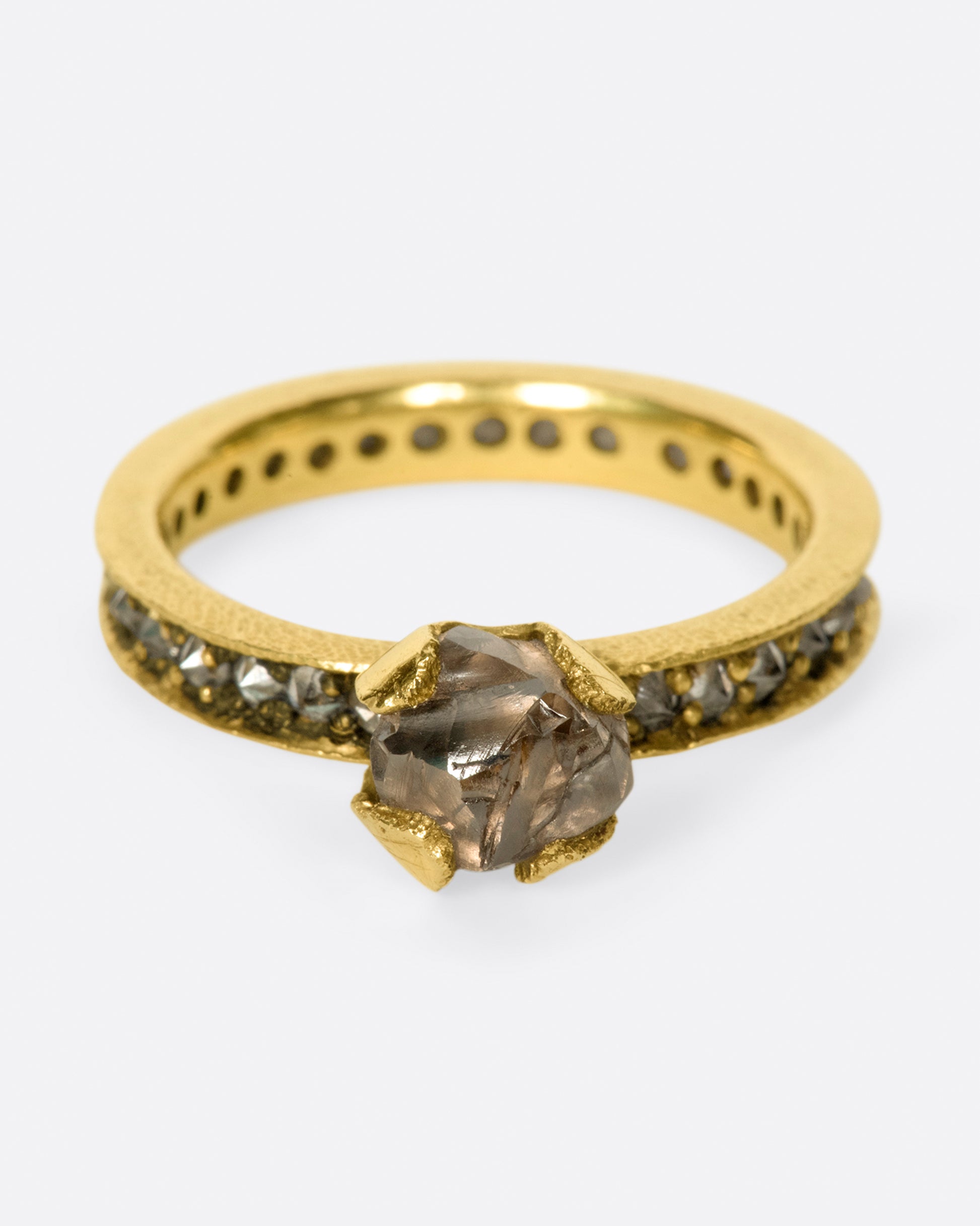 A yellow gold eternity band with inverted diamonds, crowned by a prong set raw yellow diamond. Shown from the front.
