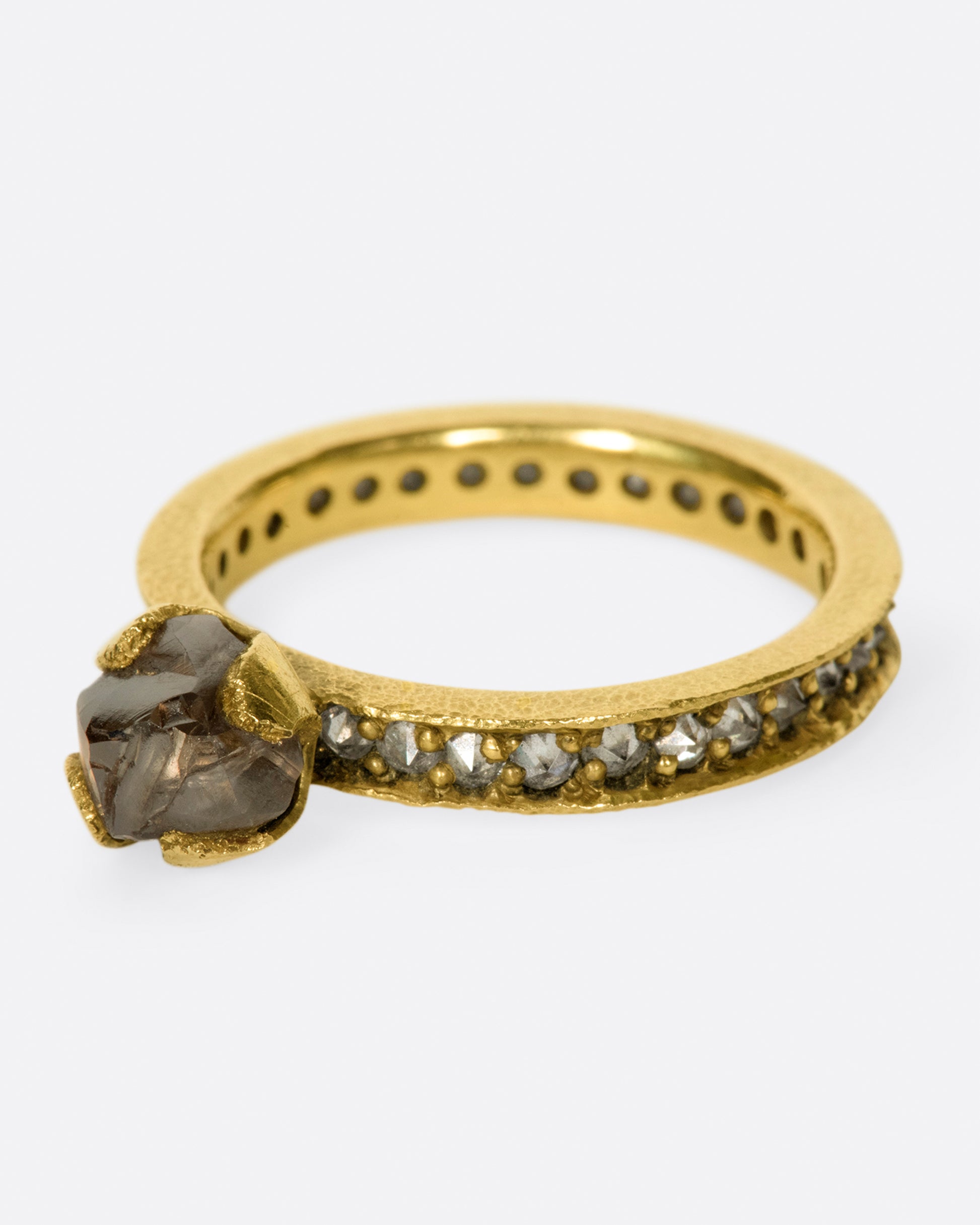 A yellow gold eternity band with inverted diamonds, crowned by a prong set raw yellow diamond. Shown from the side.