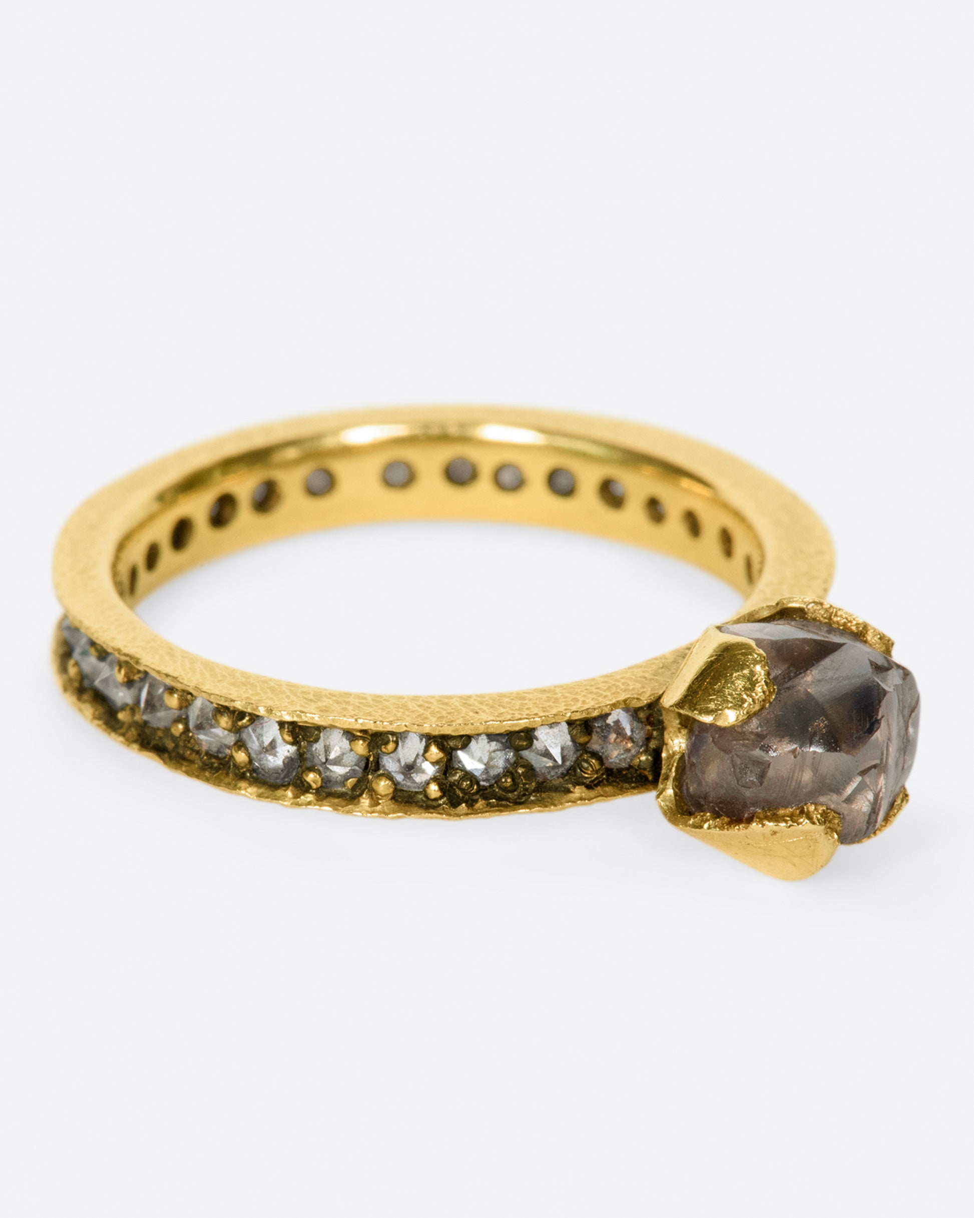 A yellow gold eternity band with inverted diamonds, crowned by a prong set raw yellow diamond. Shown from the side.