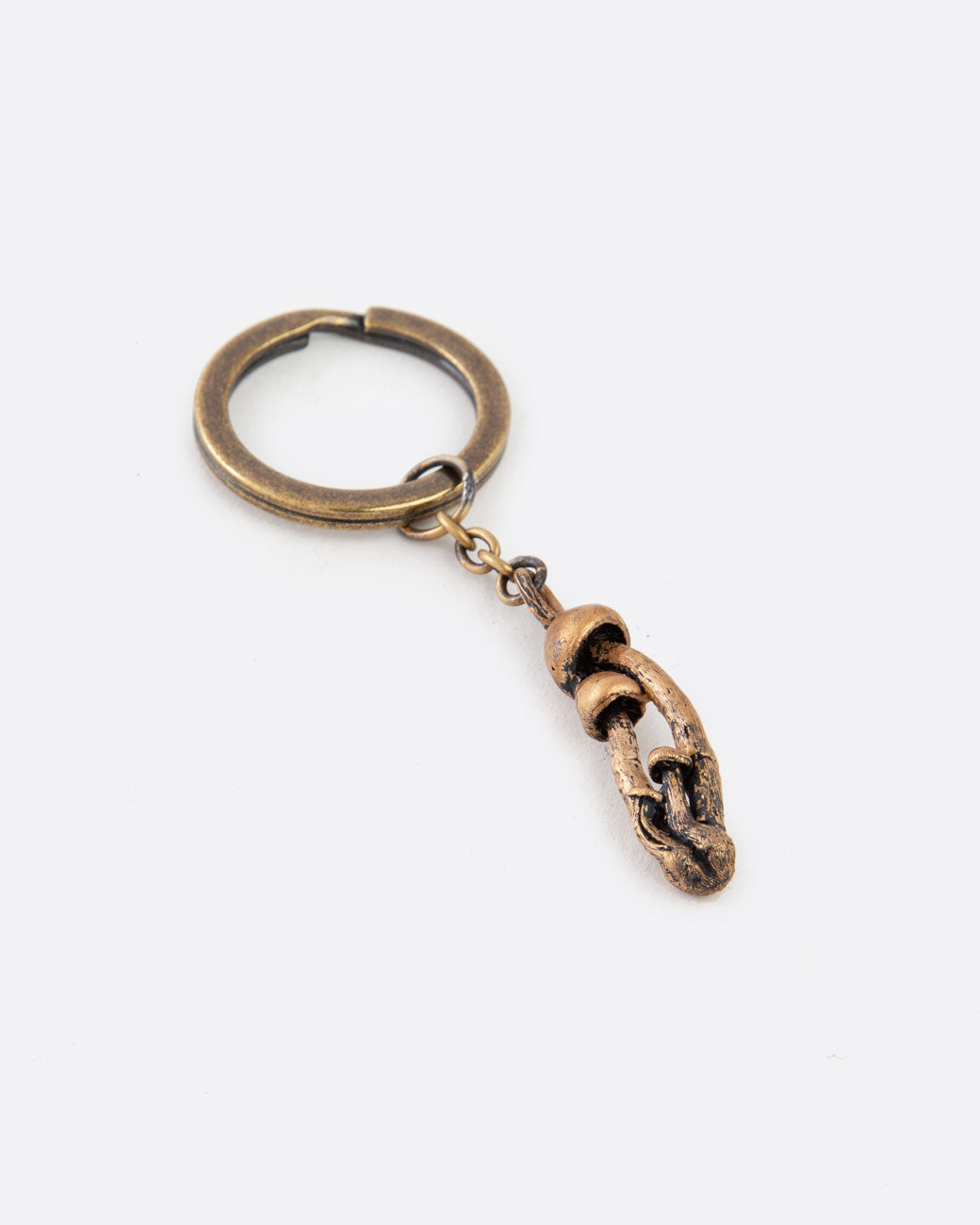 A bronze keychain with a cluster of mushrooms. Shown lying flat at an angle.